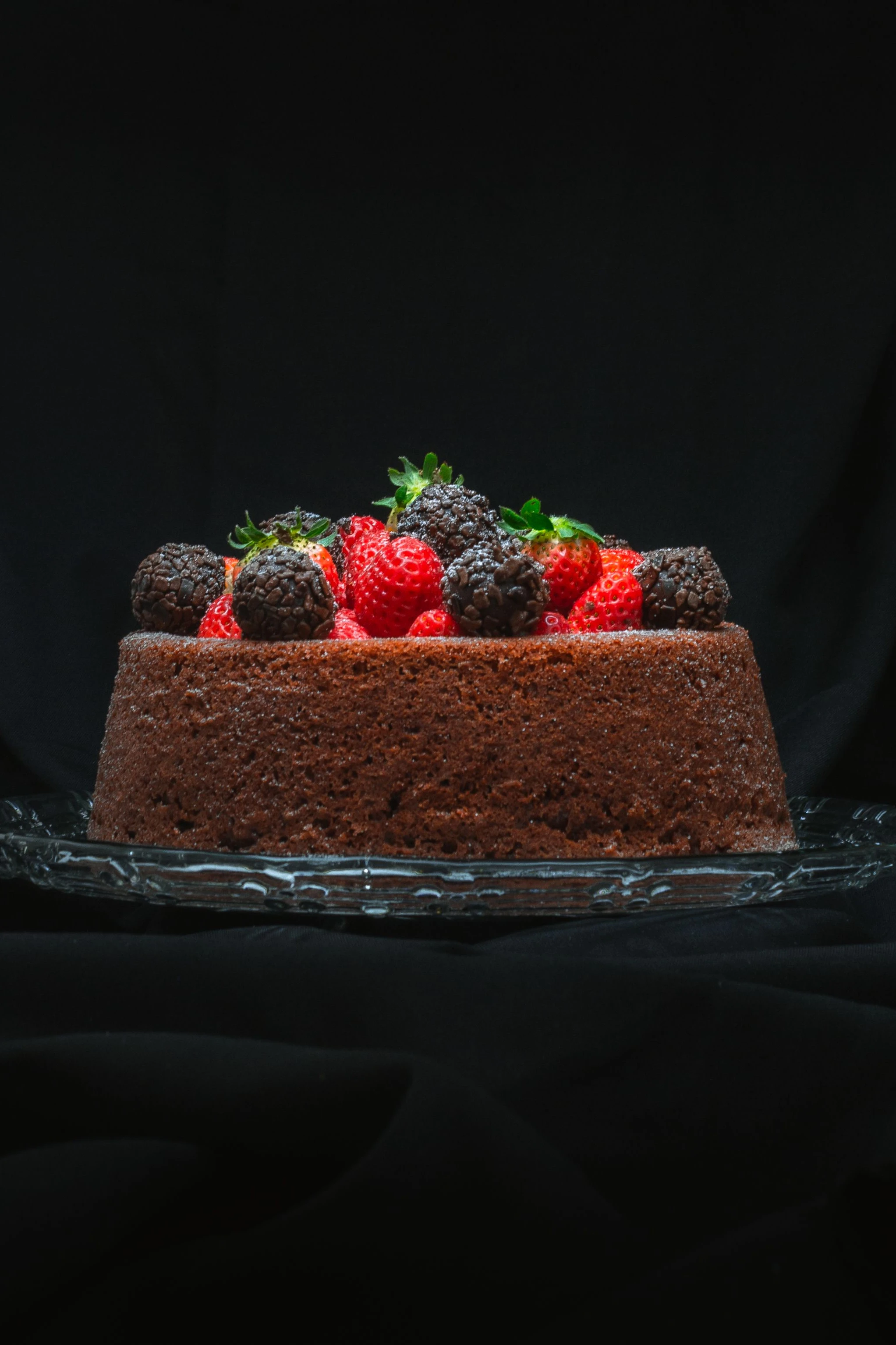 A slice of chocolate cake topped with bright berries on a dark plate in Curitiba.