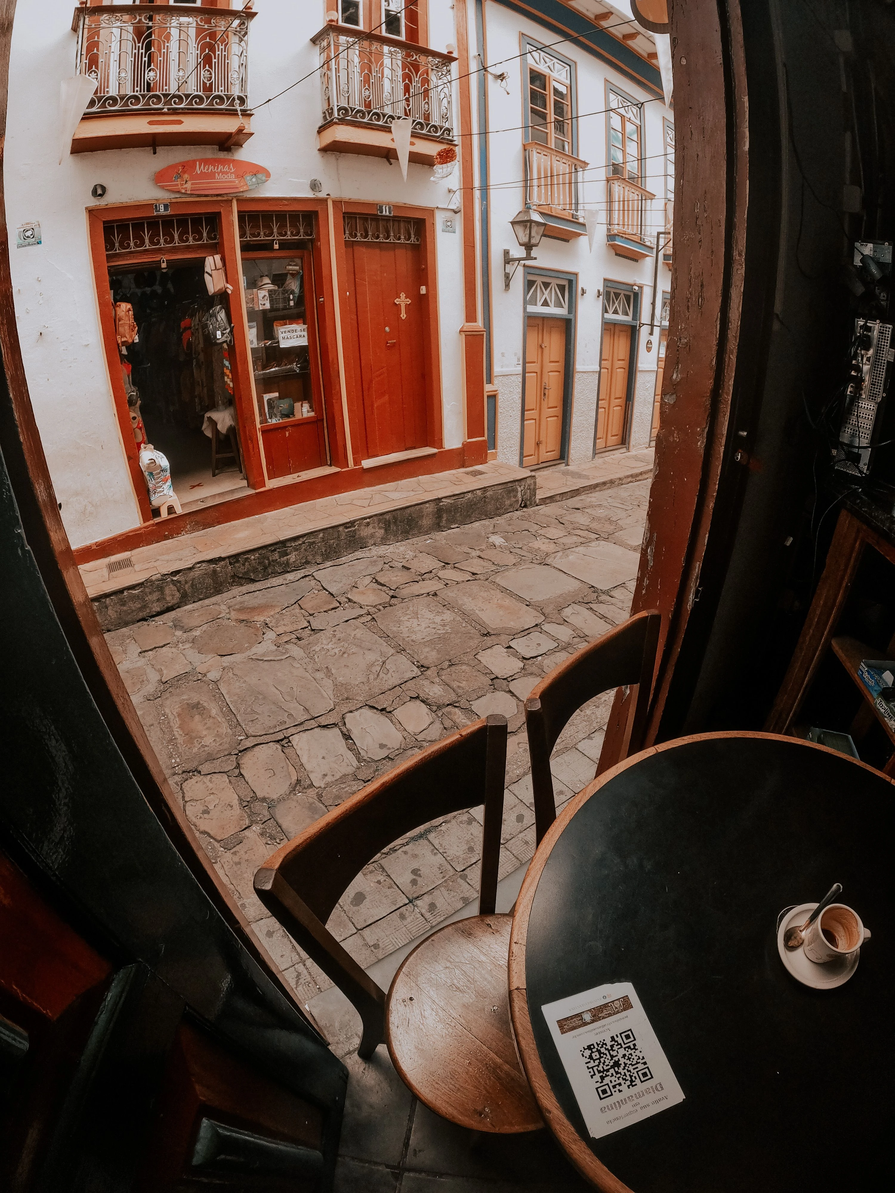 A café table with coffee and a QR menu beside a window overlooking Diamantina