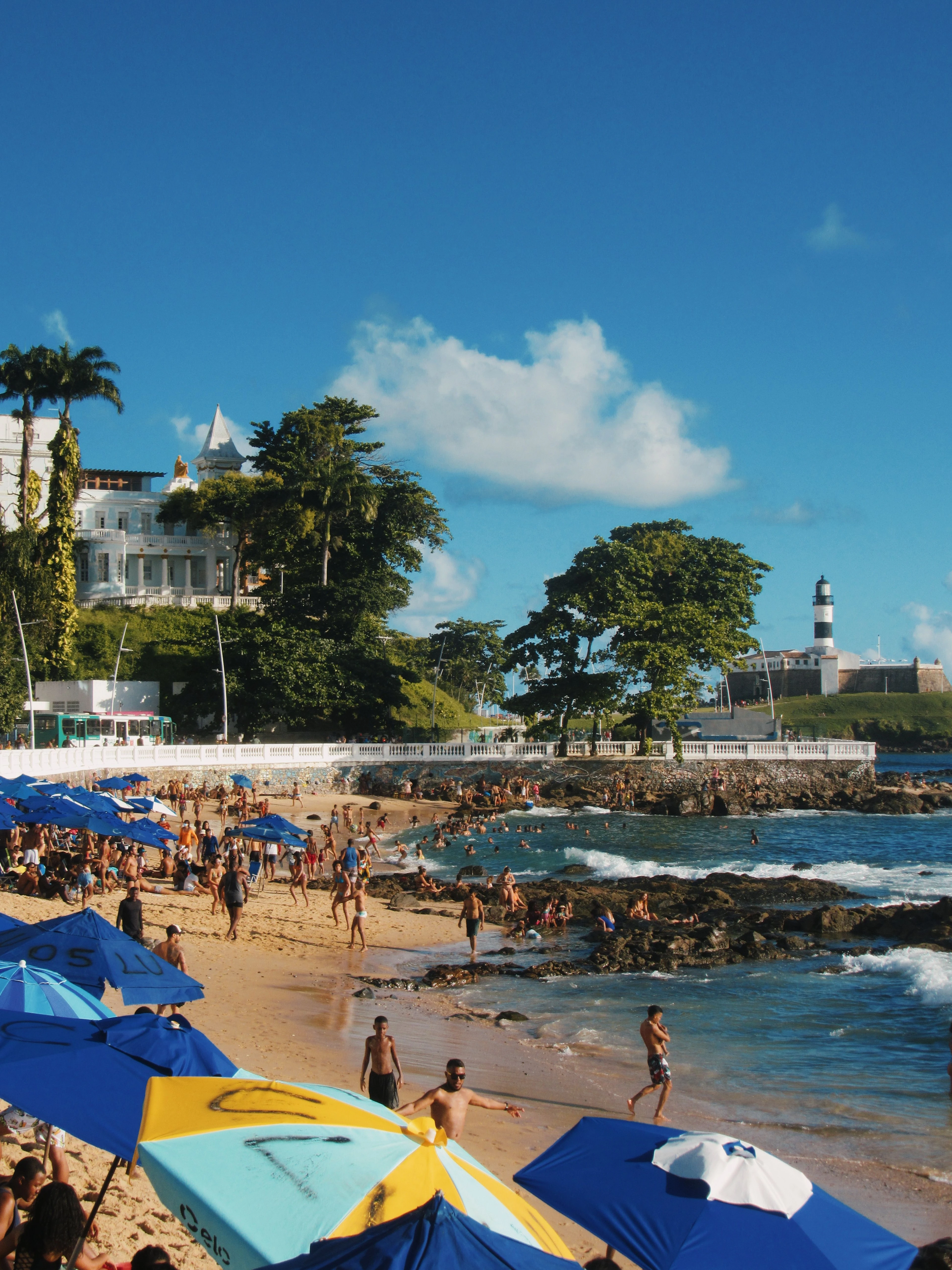 Beachgoers and colorful umbrellas fill the shoreline beneath Farol da Barra