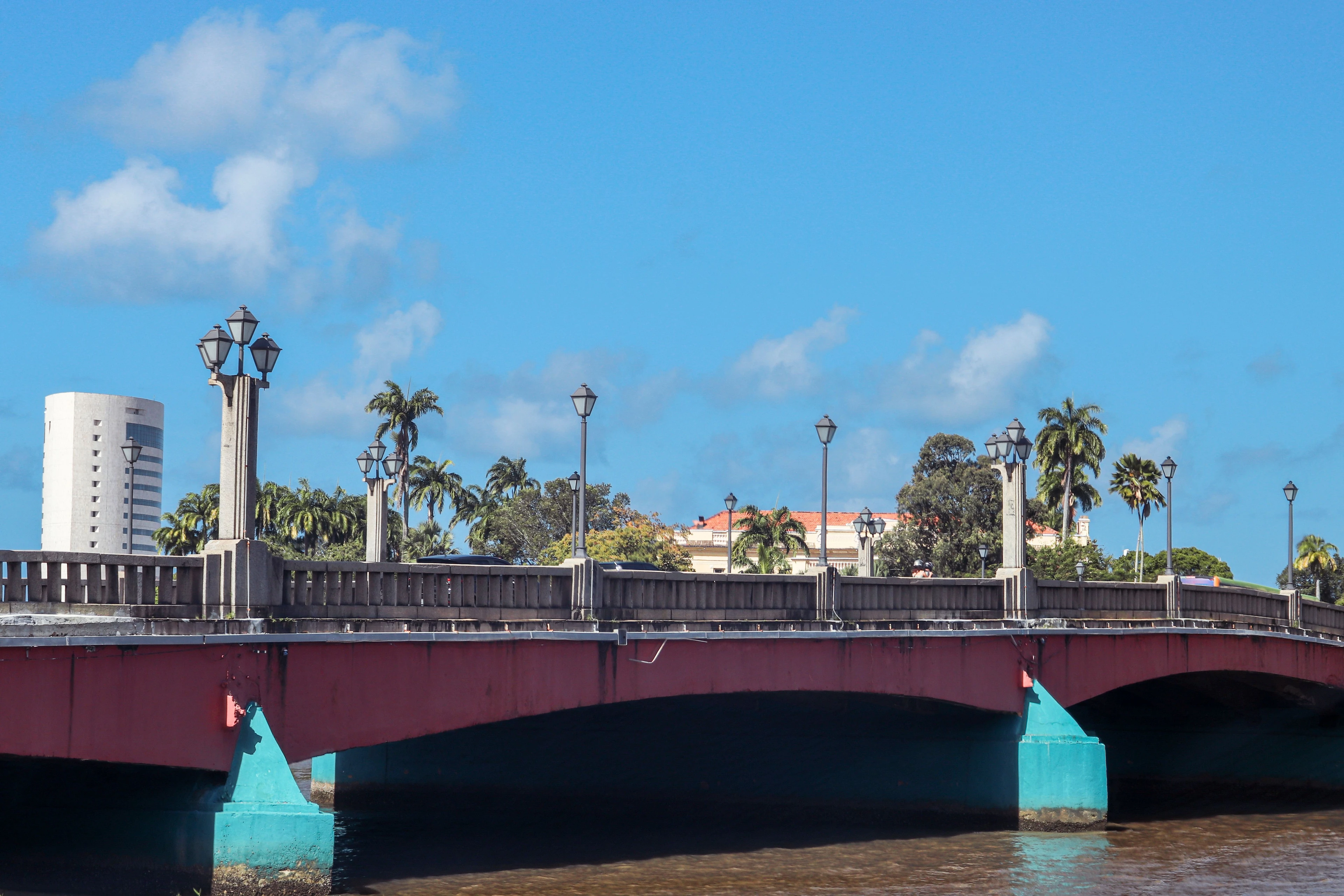 A colorful red and turquoise bridge crosses Recife’s river under a bright blue sky