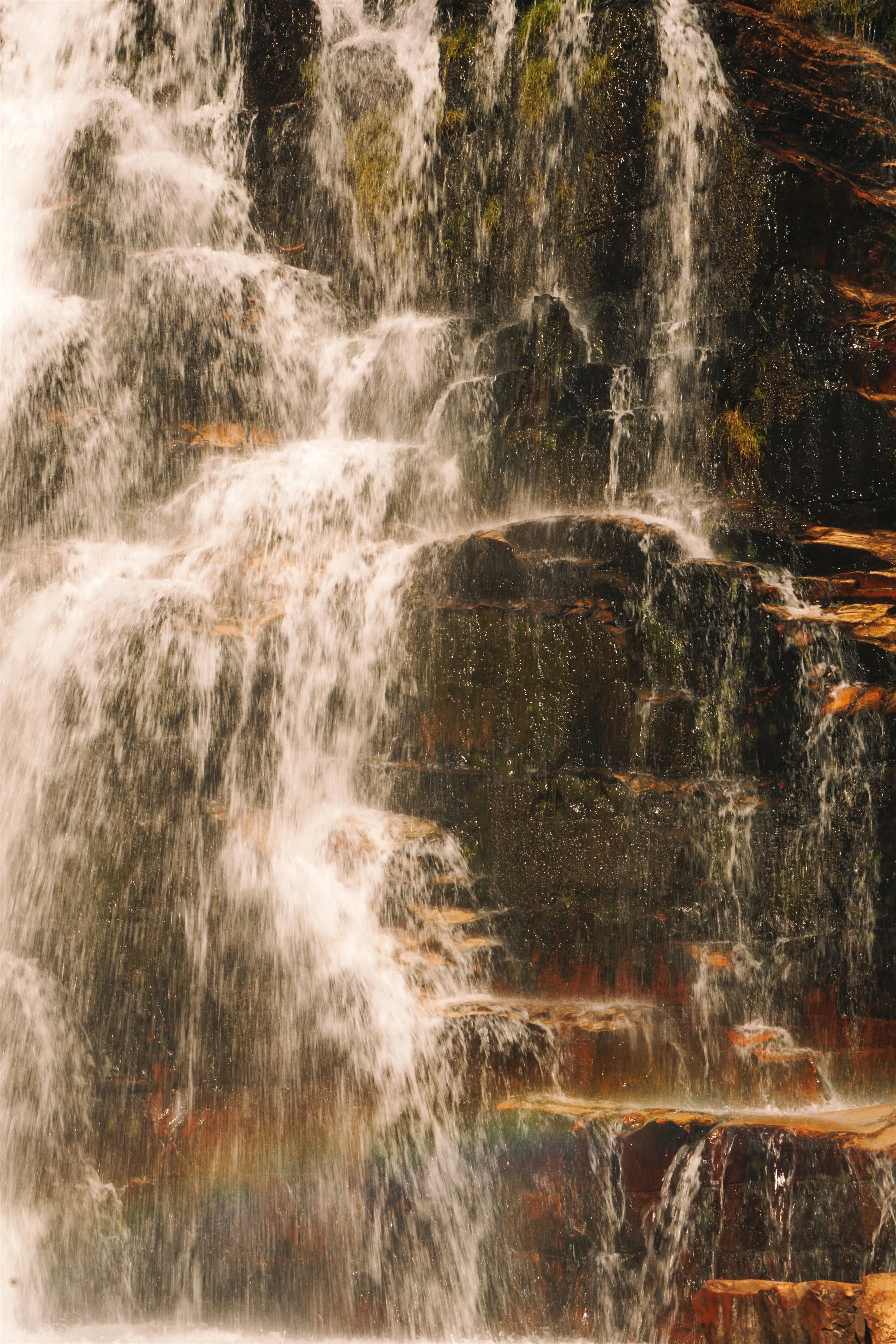 A waterfall and rainbow in the spray beside sharply layered rock in Alto Paraíso de Goiás.