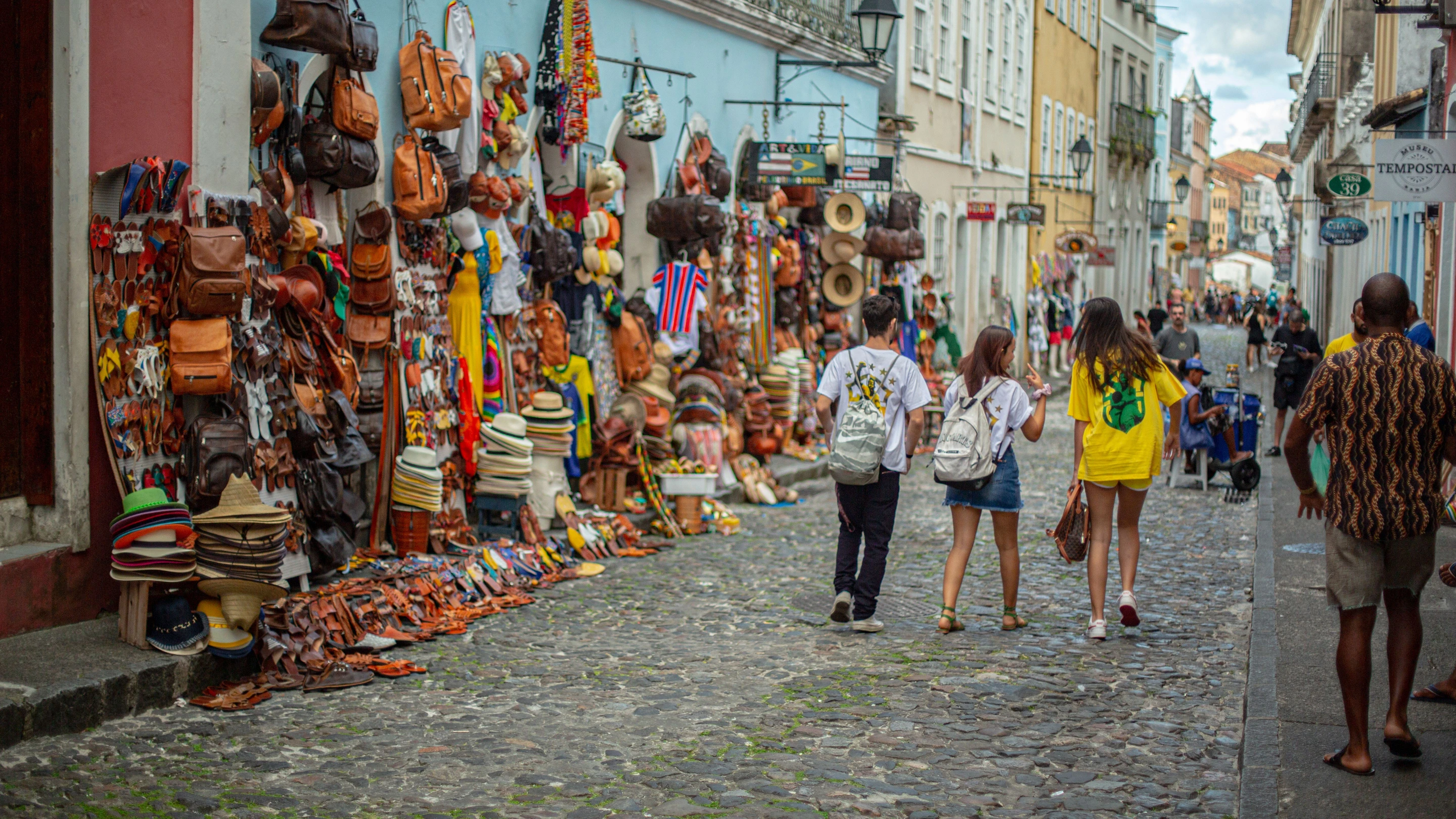 People pass shops and colorful leather goods along a historic Salvador street