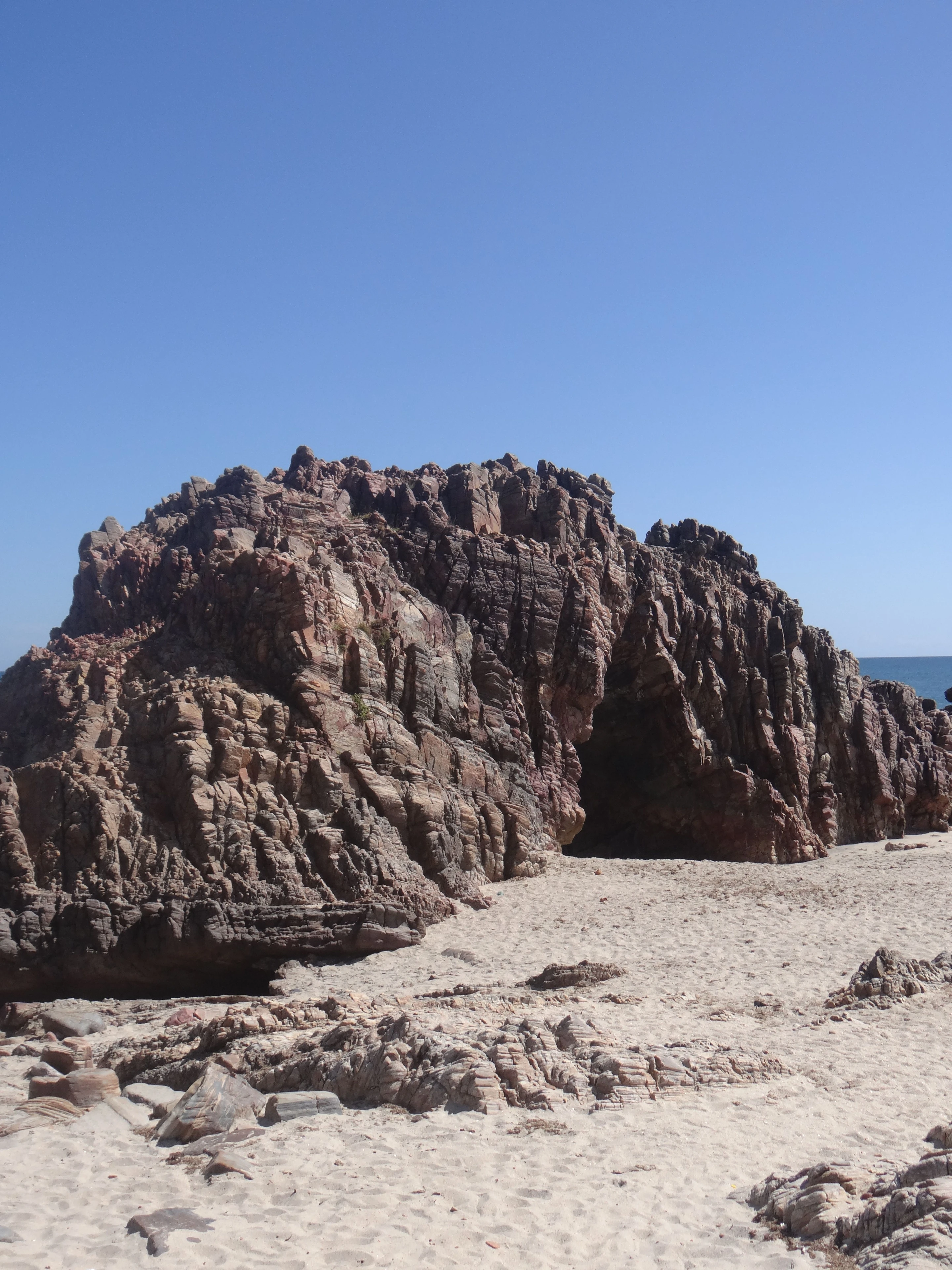 Rugged coastal rock formations rise from pale sand beneath a clear blue sky in Jericoacoara