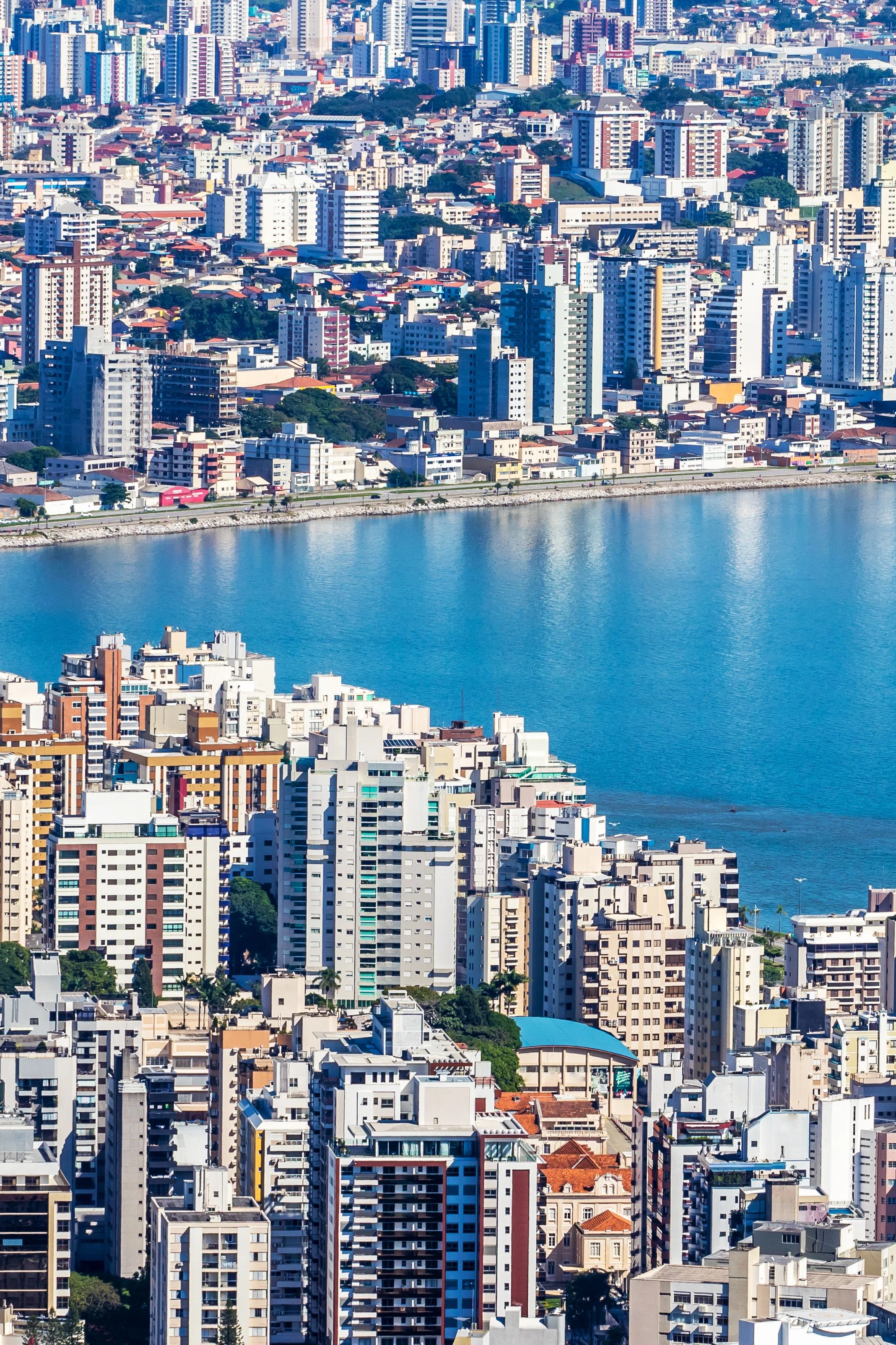 Dense city buildings and the shoreline of Florianópolis spread beside the blue waters of the North Bay.