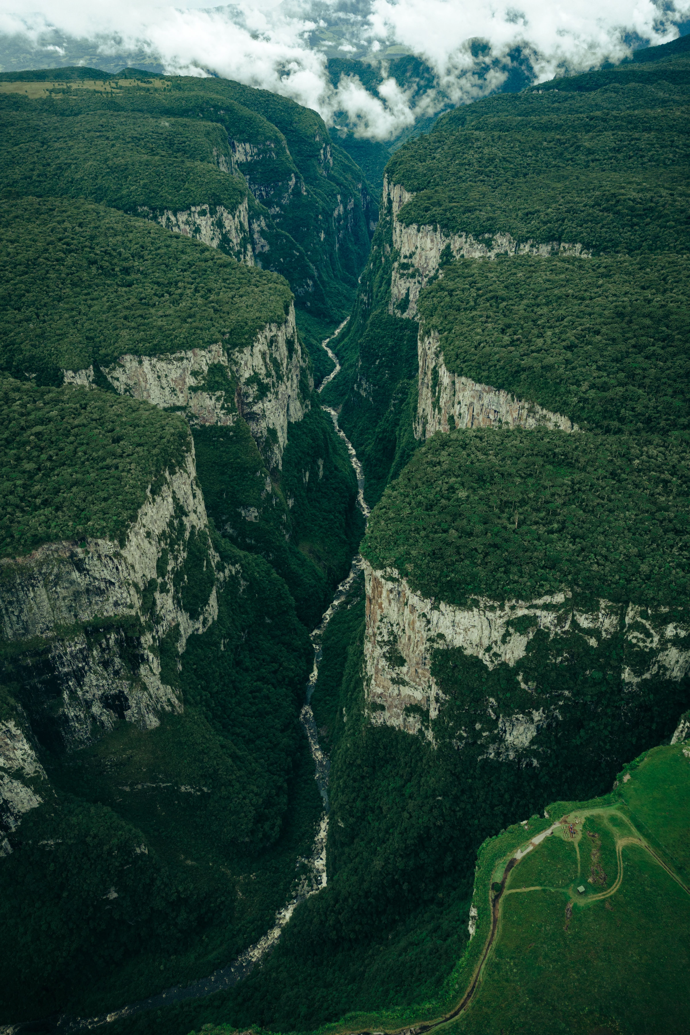 Steep forested cliffs and deep folds of the Itaimbezinho canyon beneath moving clouds.