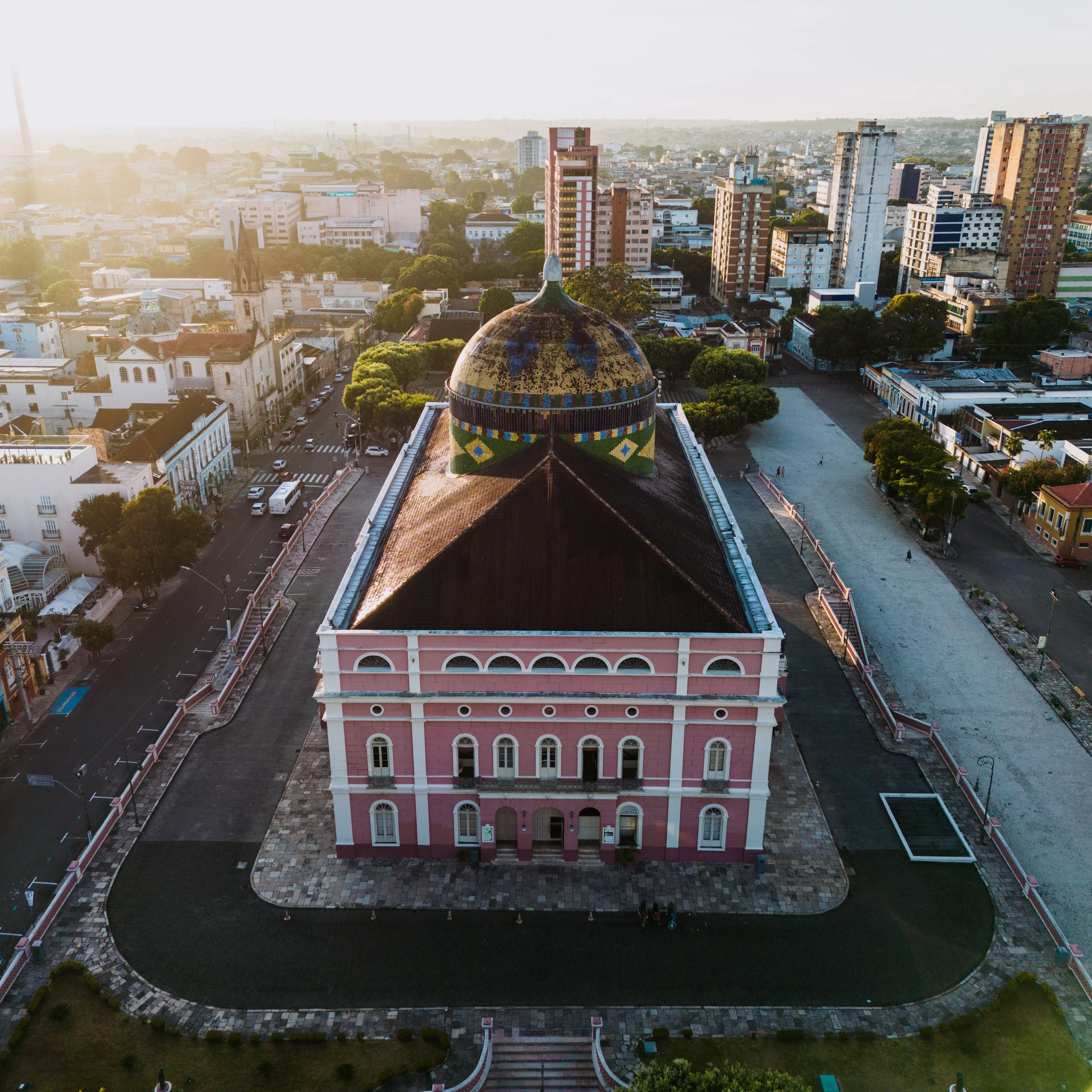 The colorful dome and pink façade of Teatro Amazonas rise above central Manaus in warm light.