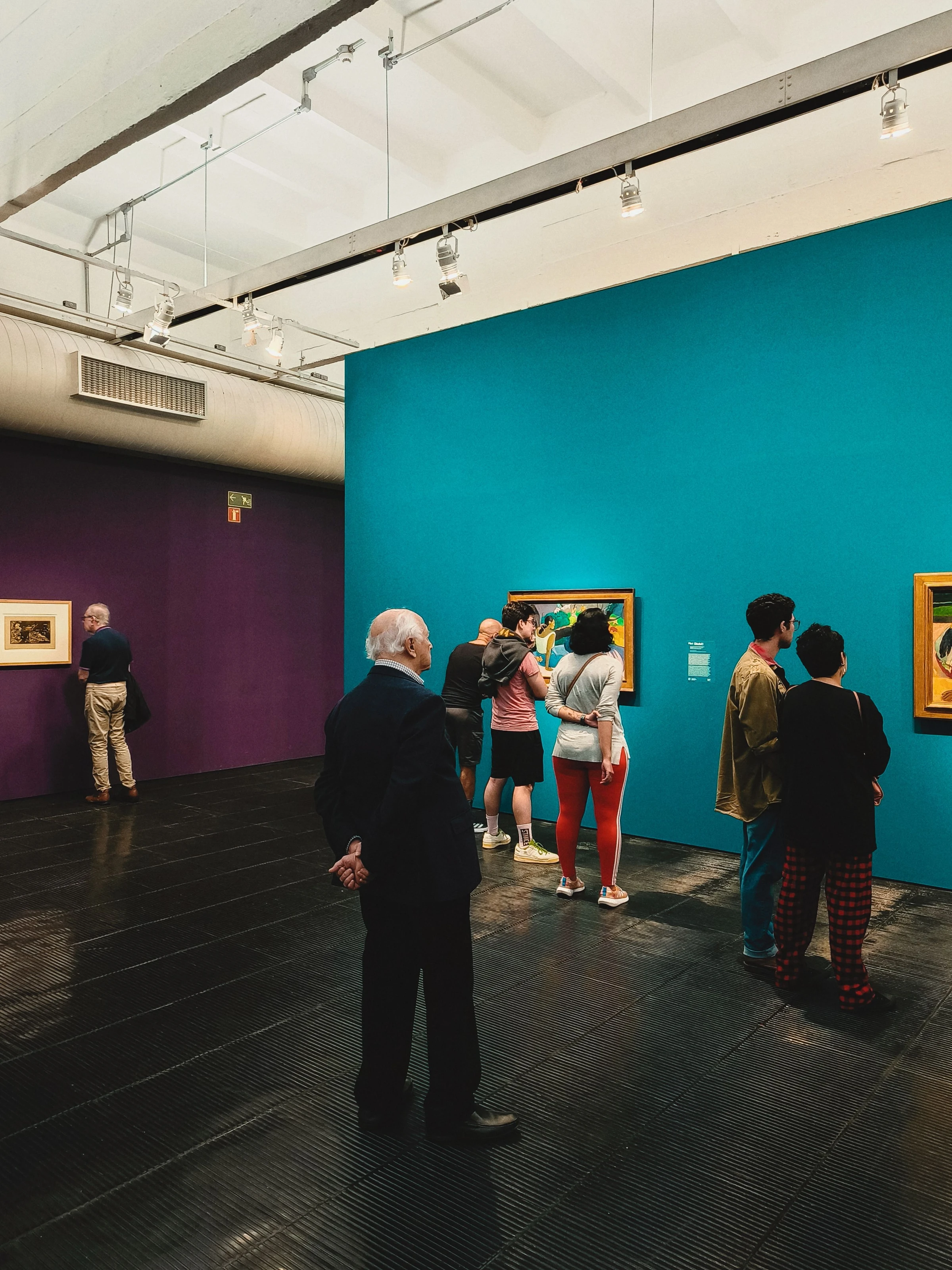 Visitors study paintings in a São Paulo art gallery with brightly colored walls.