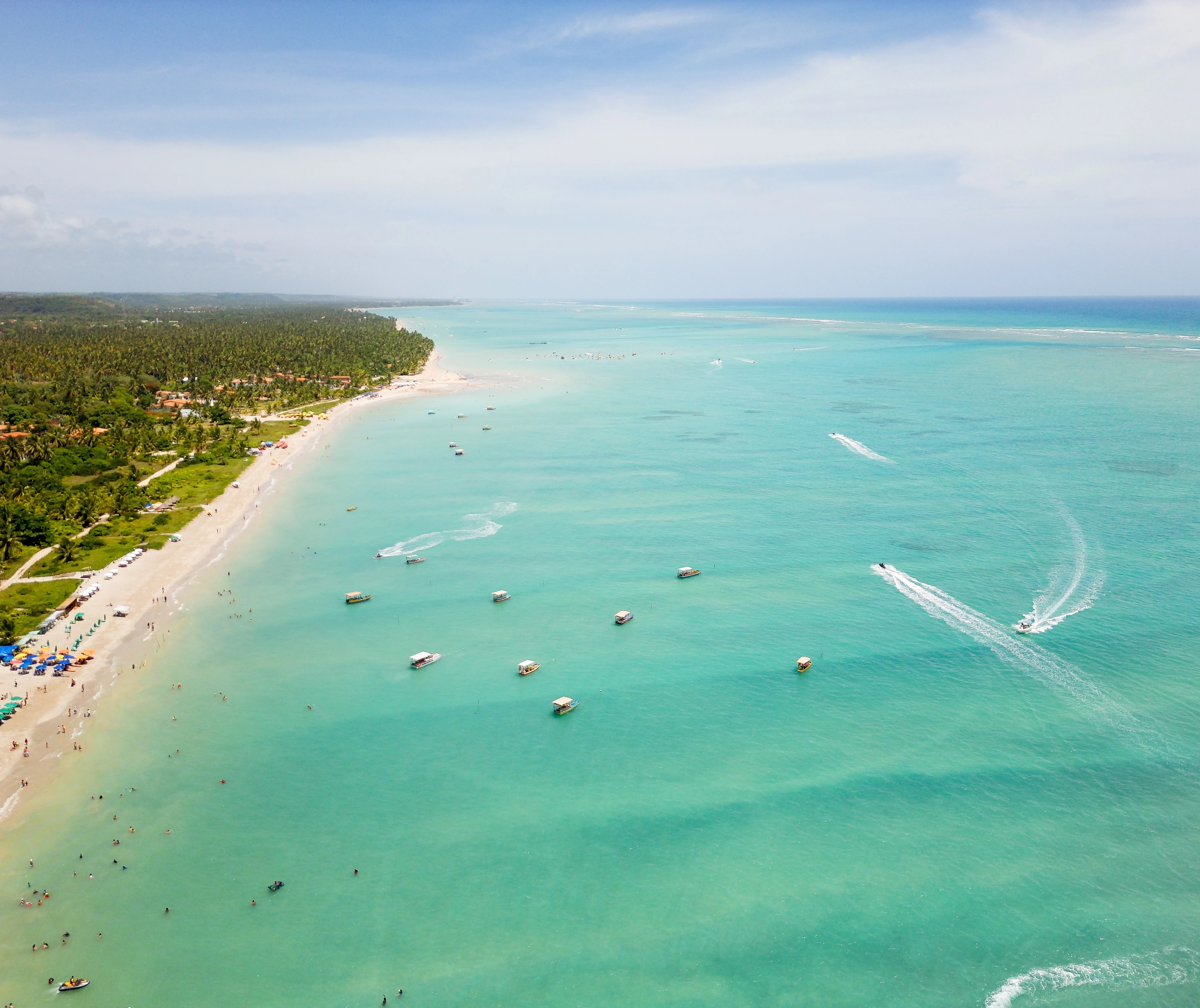 Small boats leave white wakes across the turquoise water off Antunes Beach