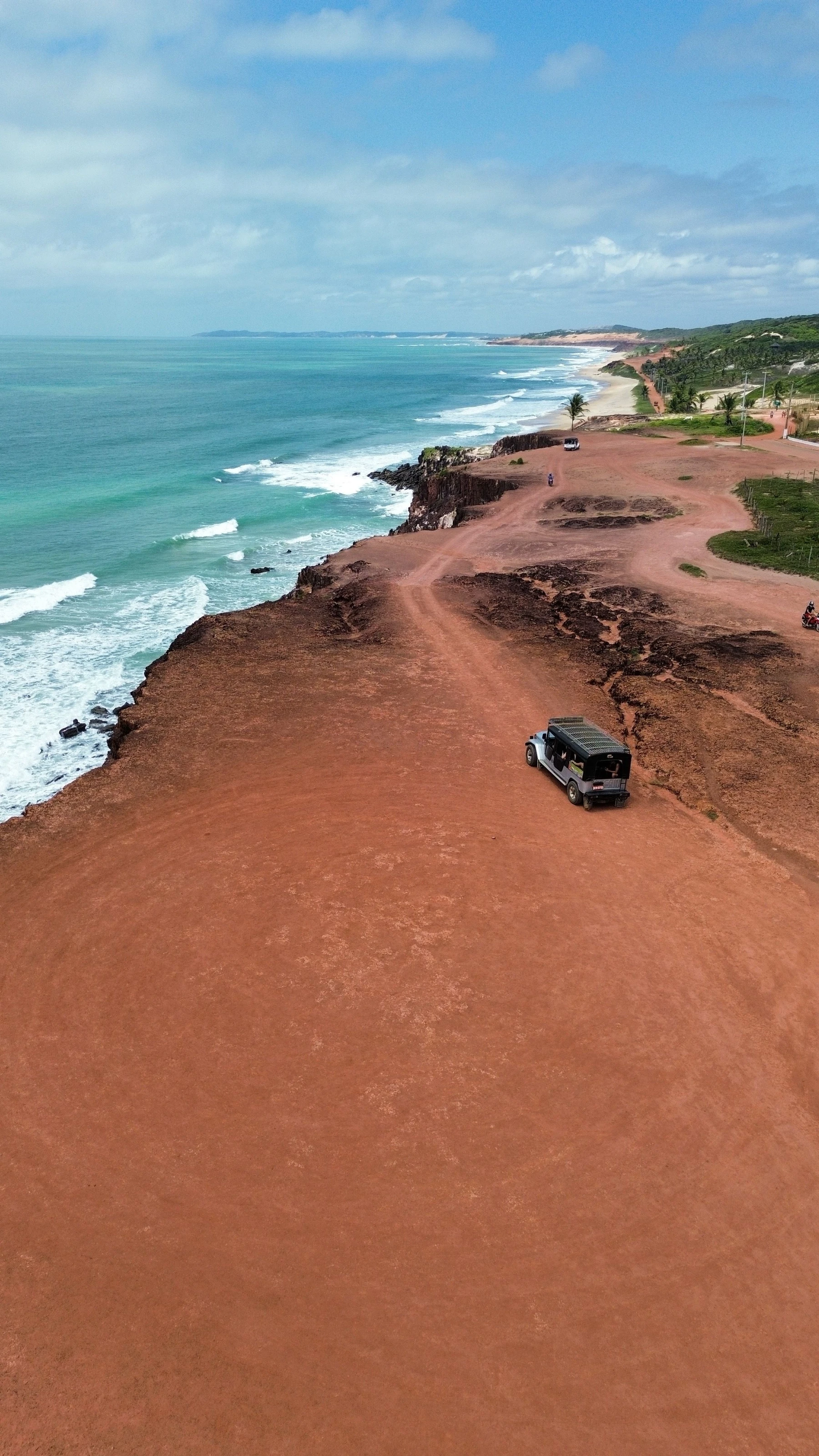 A high aerial view of red cliffs meeting blue ocean at Pipa