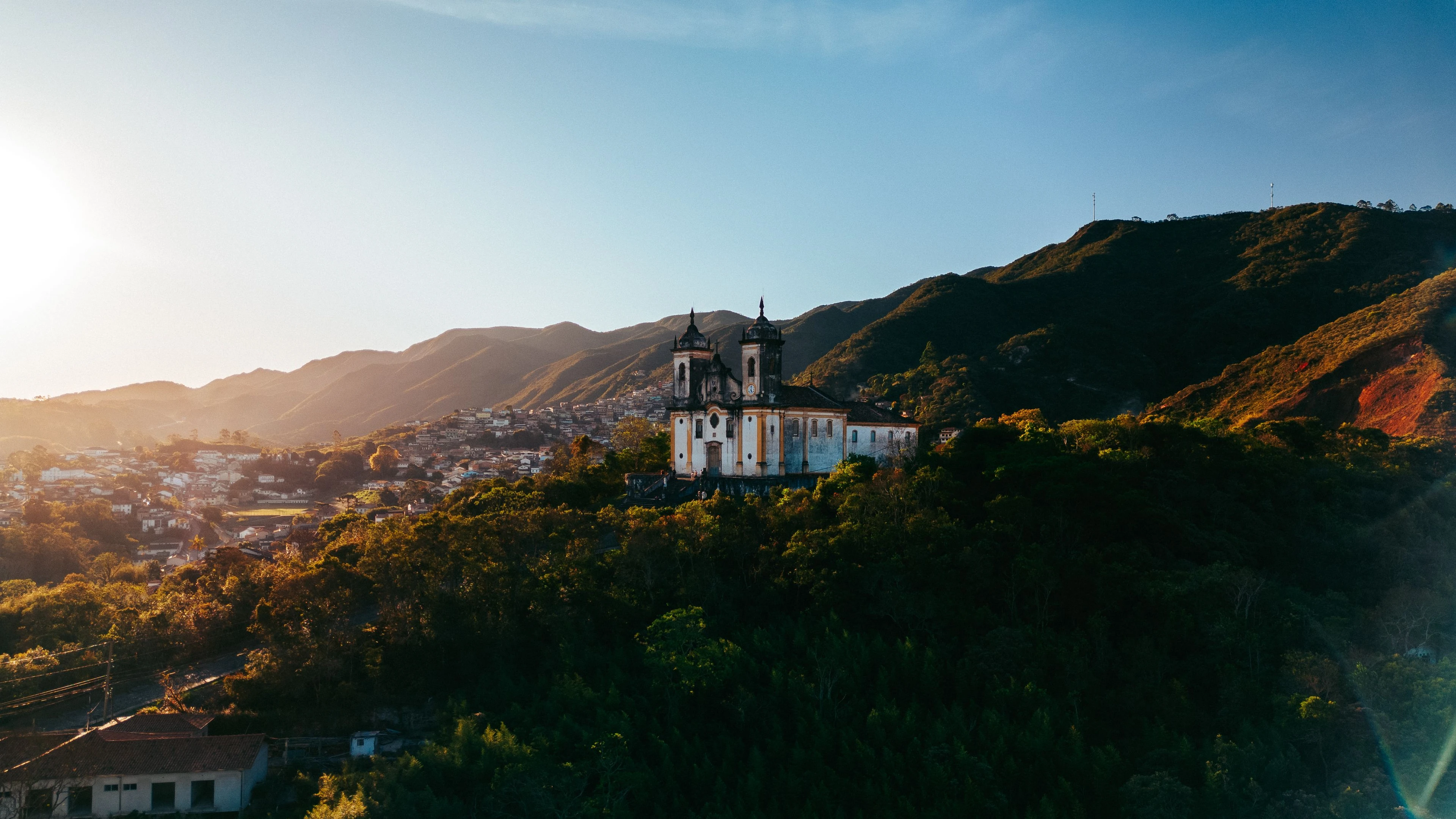 A twin-towered church above Ouro Preto in warm late-afternoon light with mountain ridges behind it