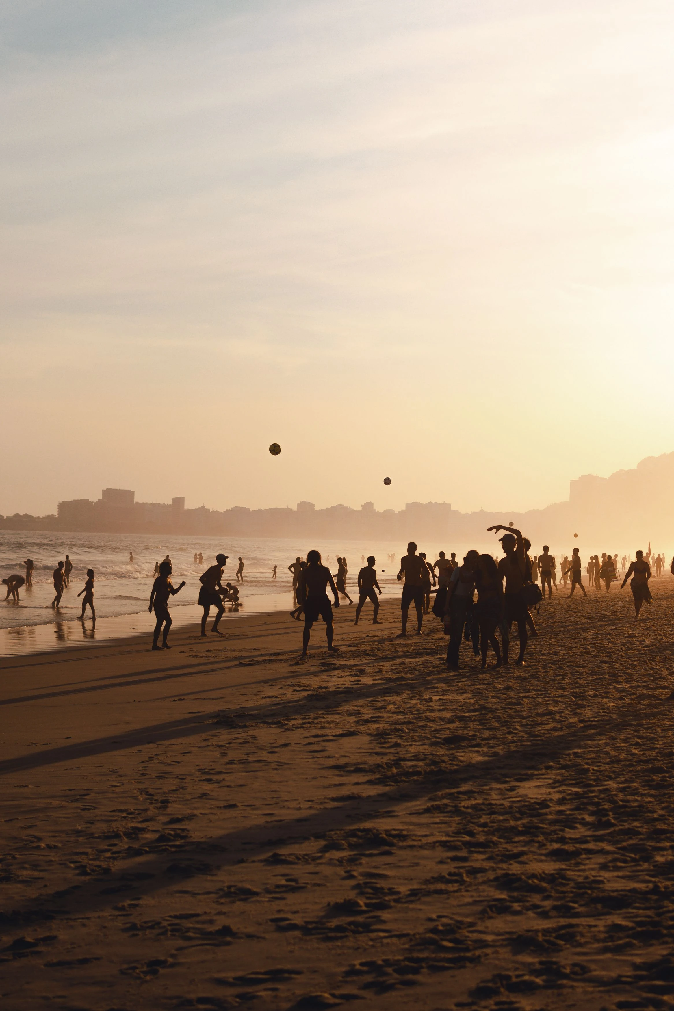 People playing ball beside the ocean in warm evening light at Ipanema