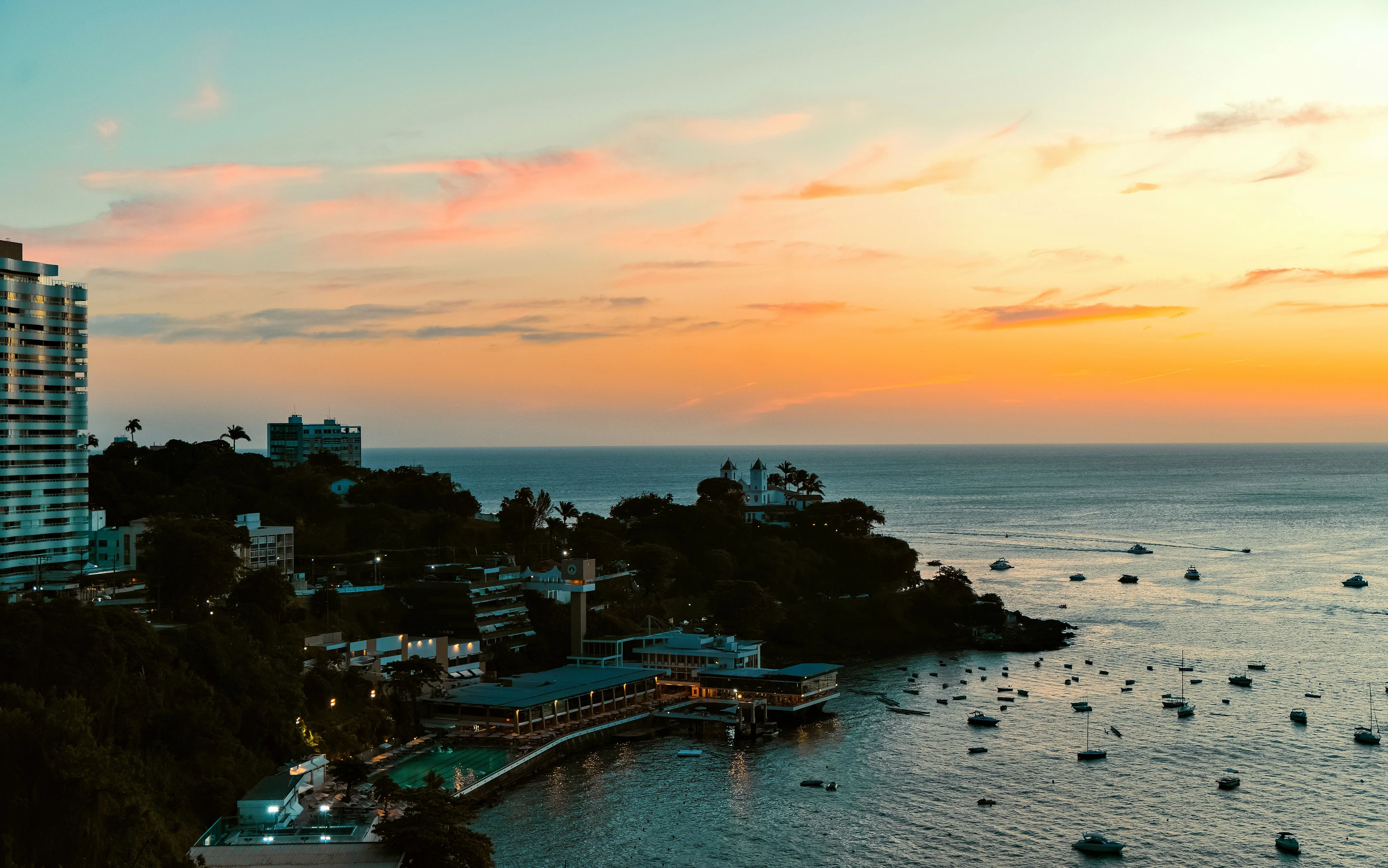 Salvador’s coastline and small boats lie beneath a gold and orange sunset.