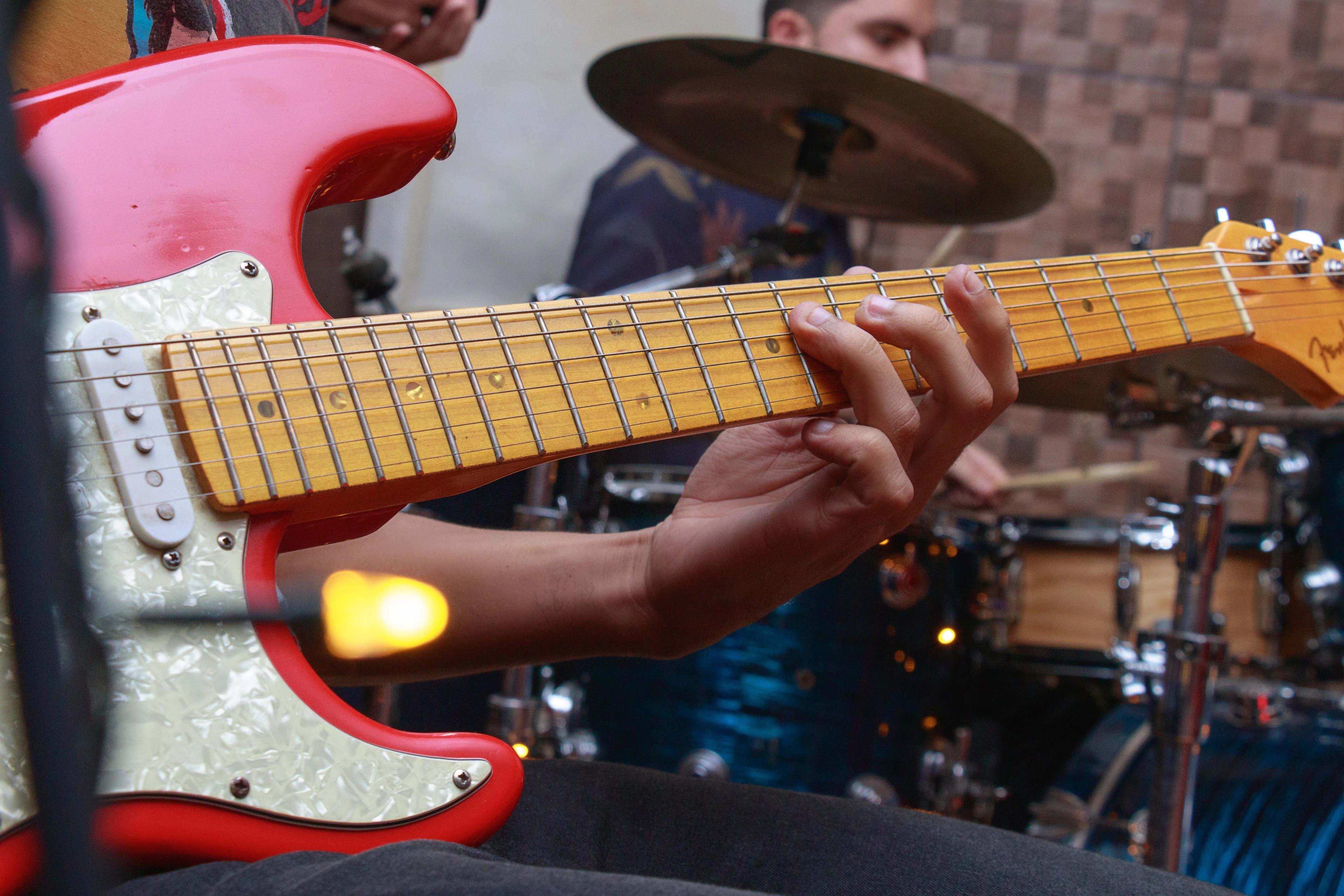 A close view of a guitarist’s hands with a drummer playing behind
