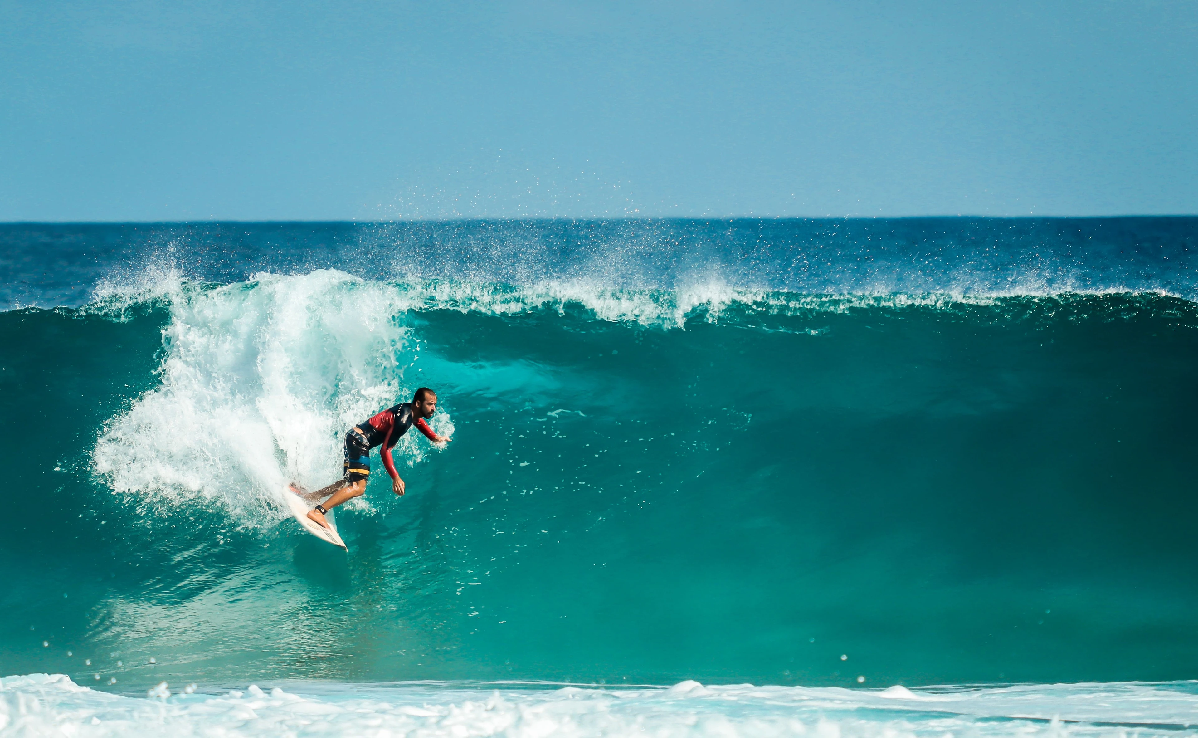 A surfer carving down the face of a turquoise wave in Fernando de Noronha