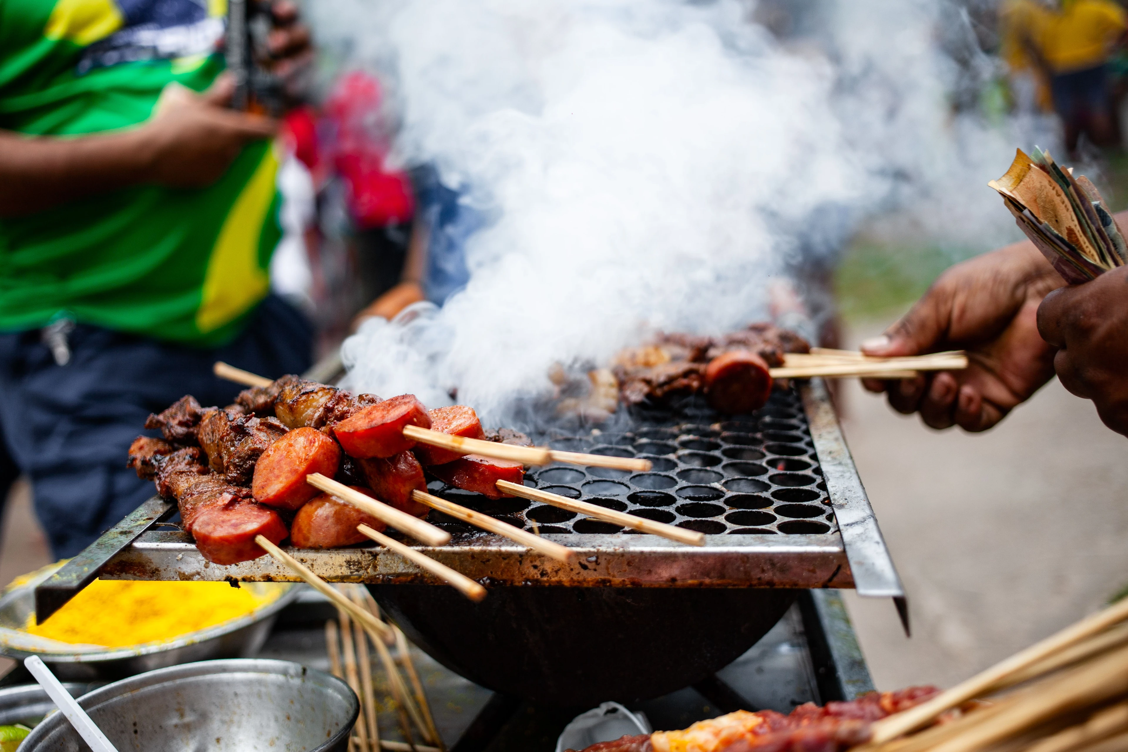 A street cook turning skewers over a smoking grill in Belém