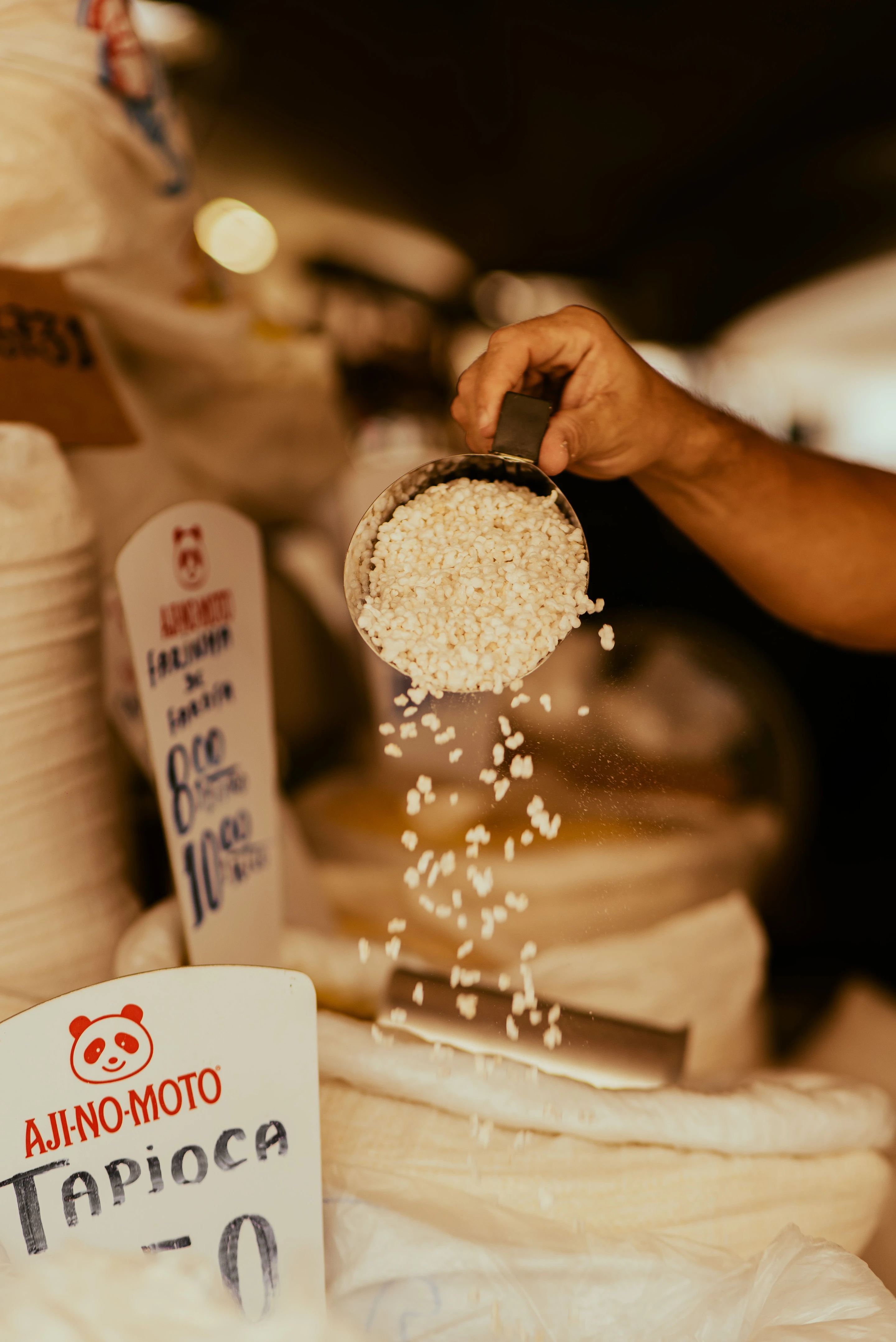 A hand scoops tapioca at a market, with grains falling back into the sack