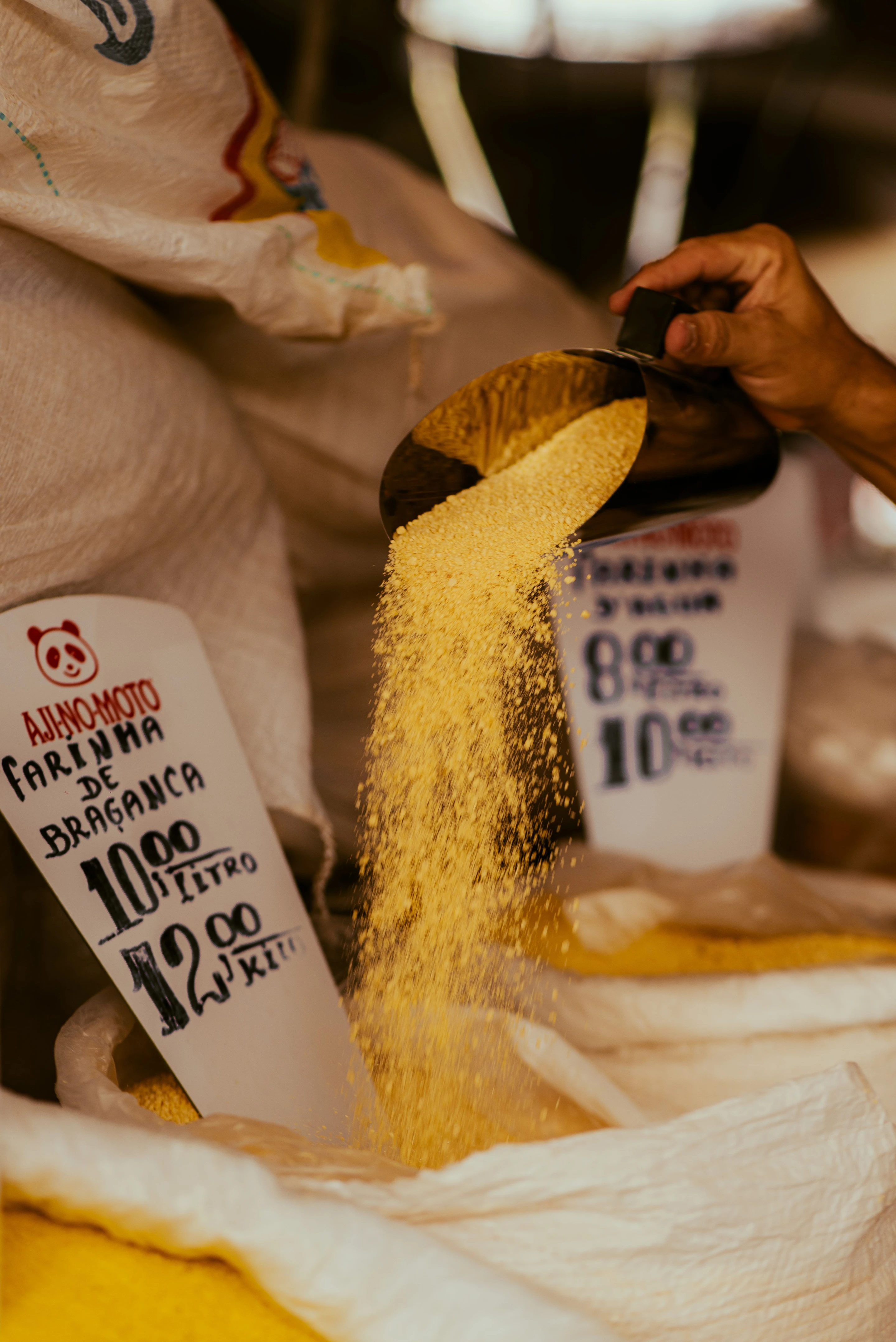 Golden Bragança manioc flour pours from a scoop into a large sack