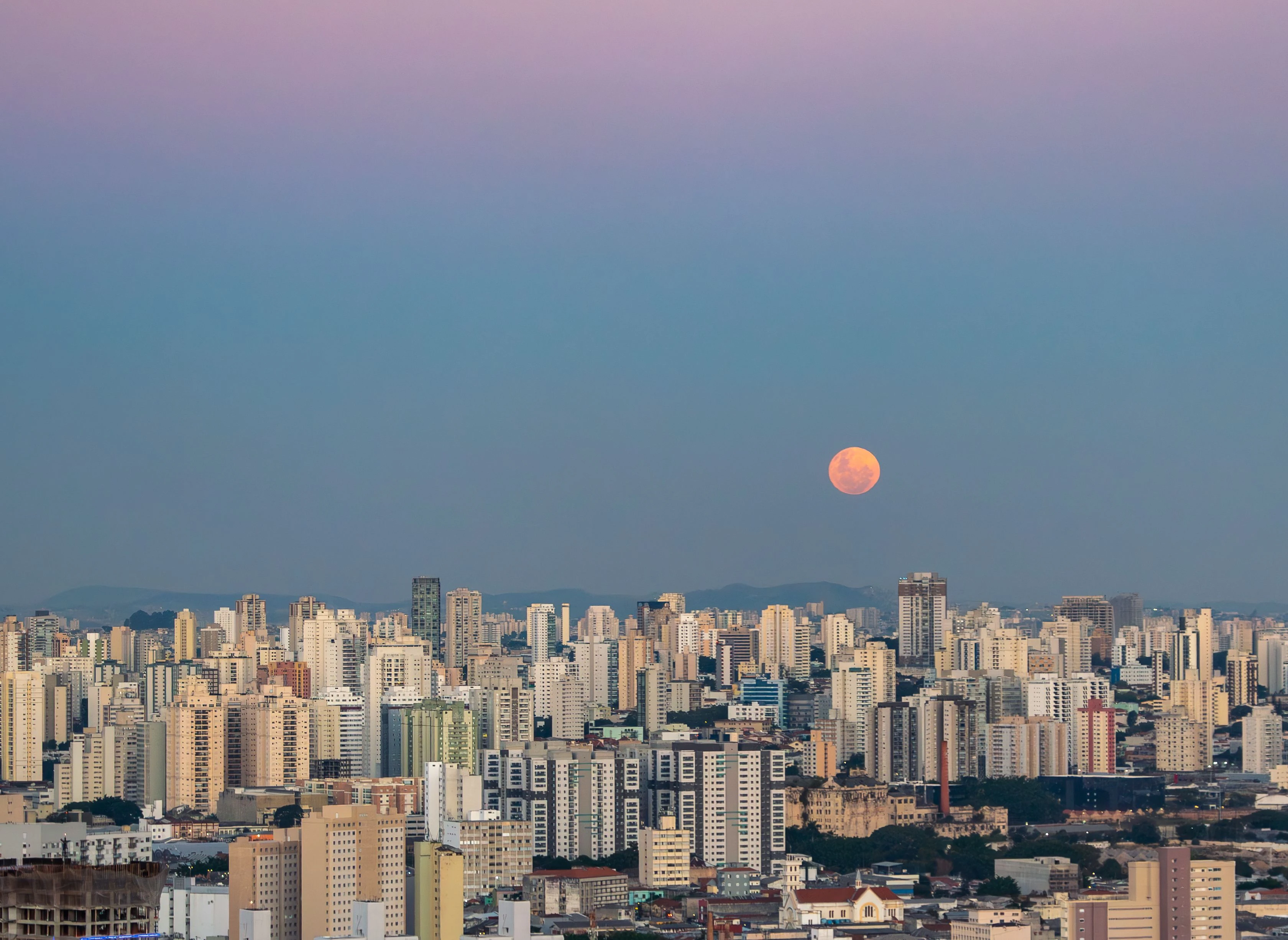An orange moon rising above a dense São Paulo skyline