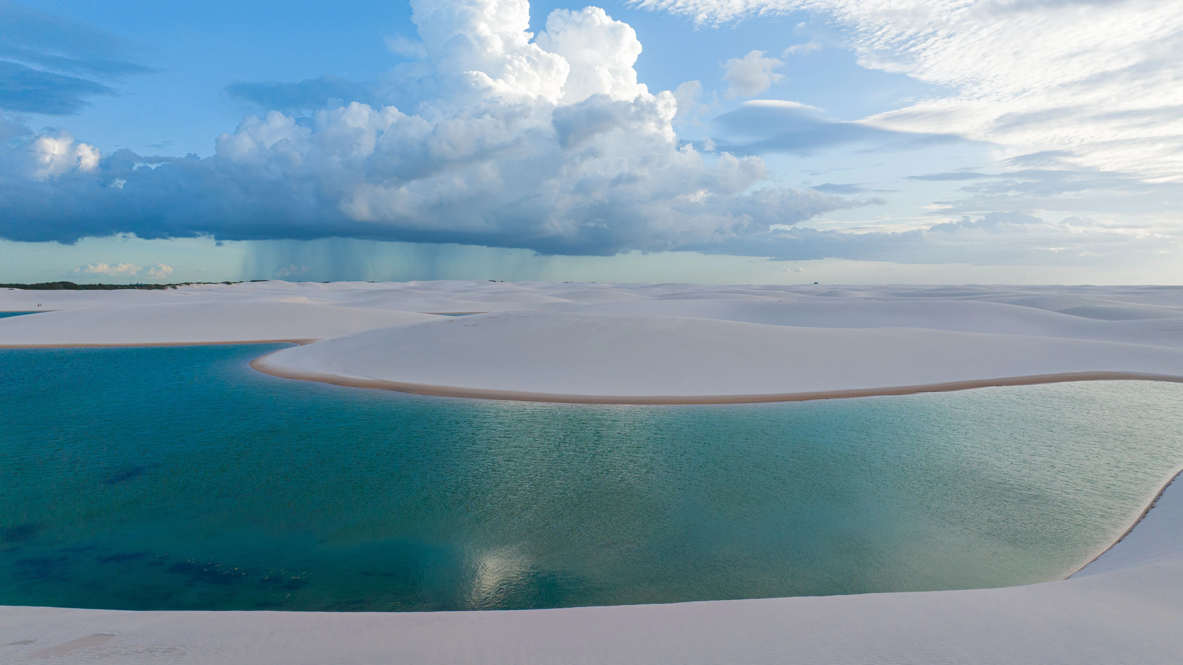 Deep blue lagoons curve between bright sand dunes beneath dramatic clouds at Lençóis Maranhenses