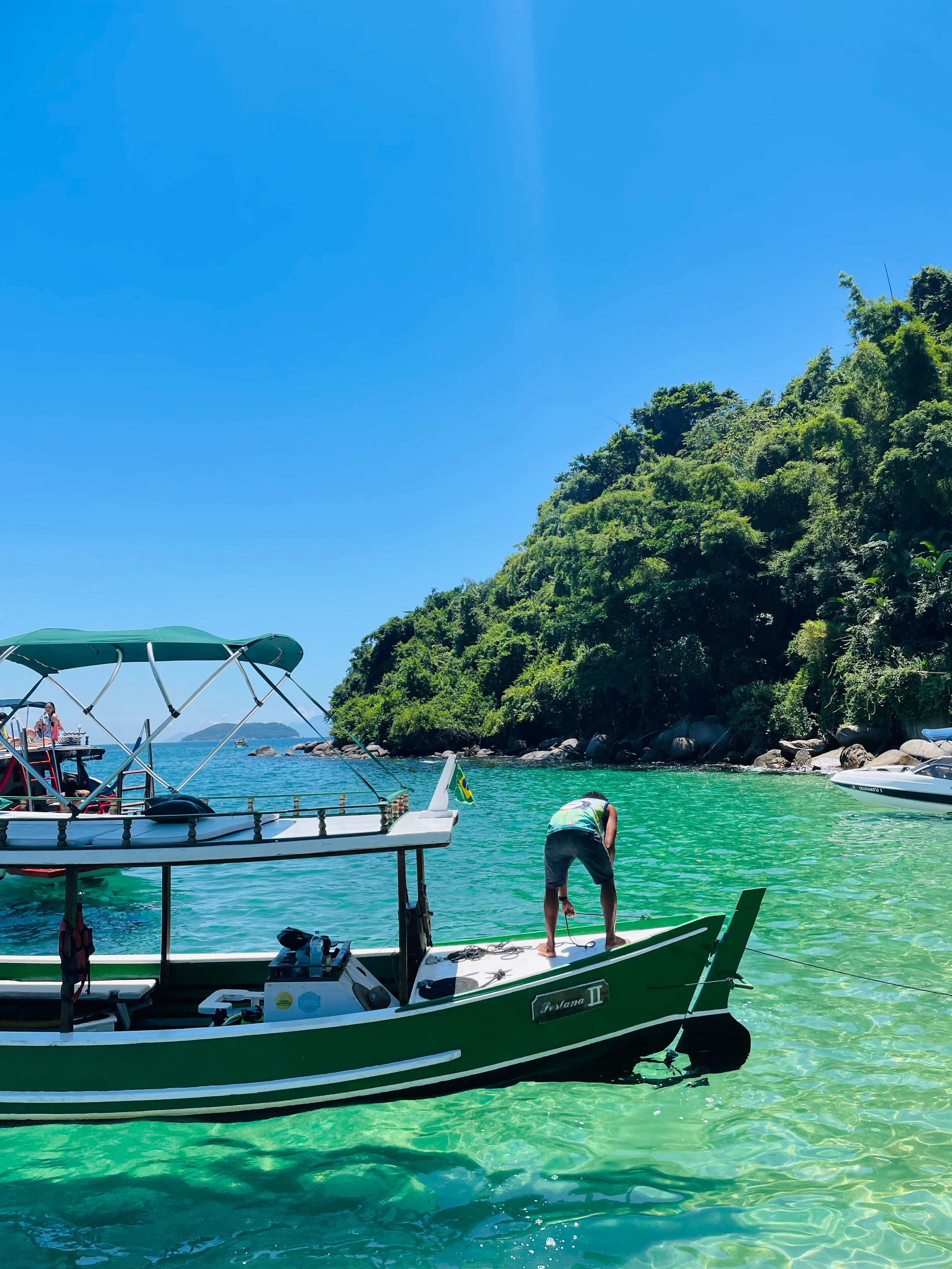 Passengers on a green boat beside the blue waters of Paraty