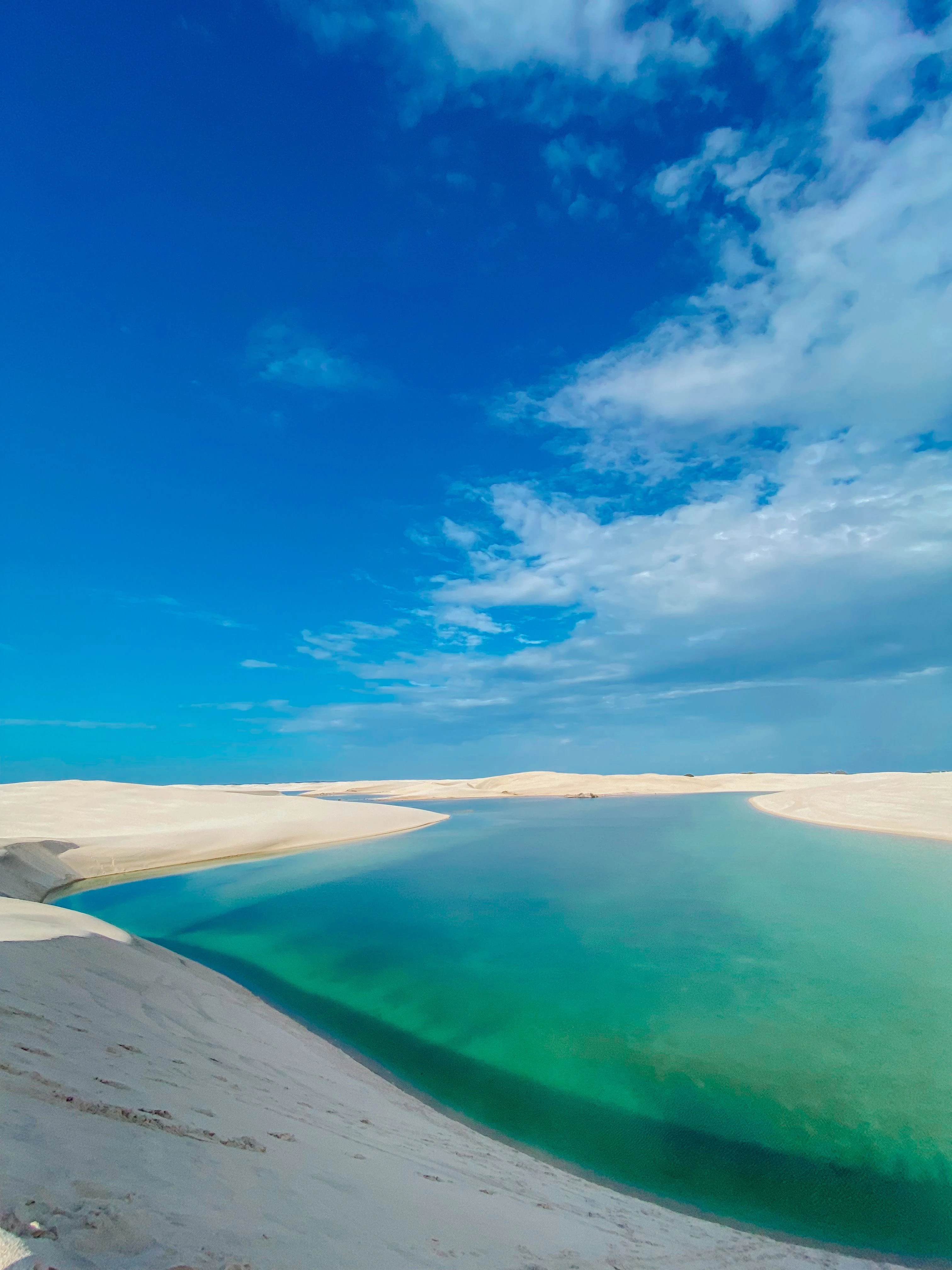 Blue lagoon enclosed by pale dunes beneath an open sky