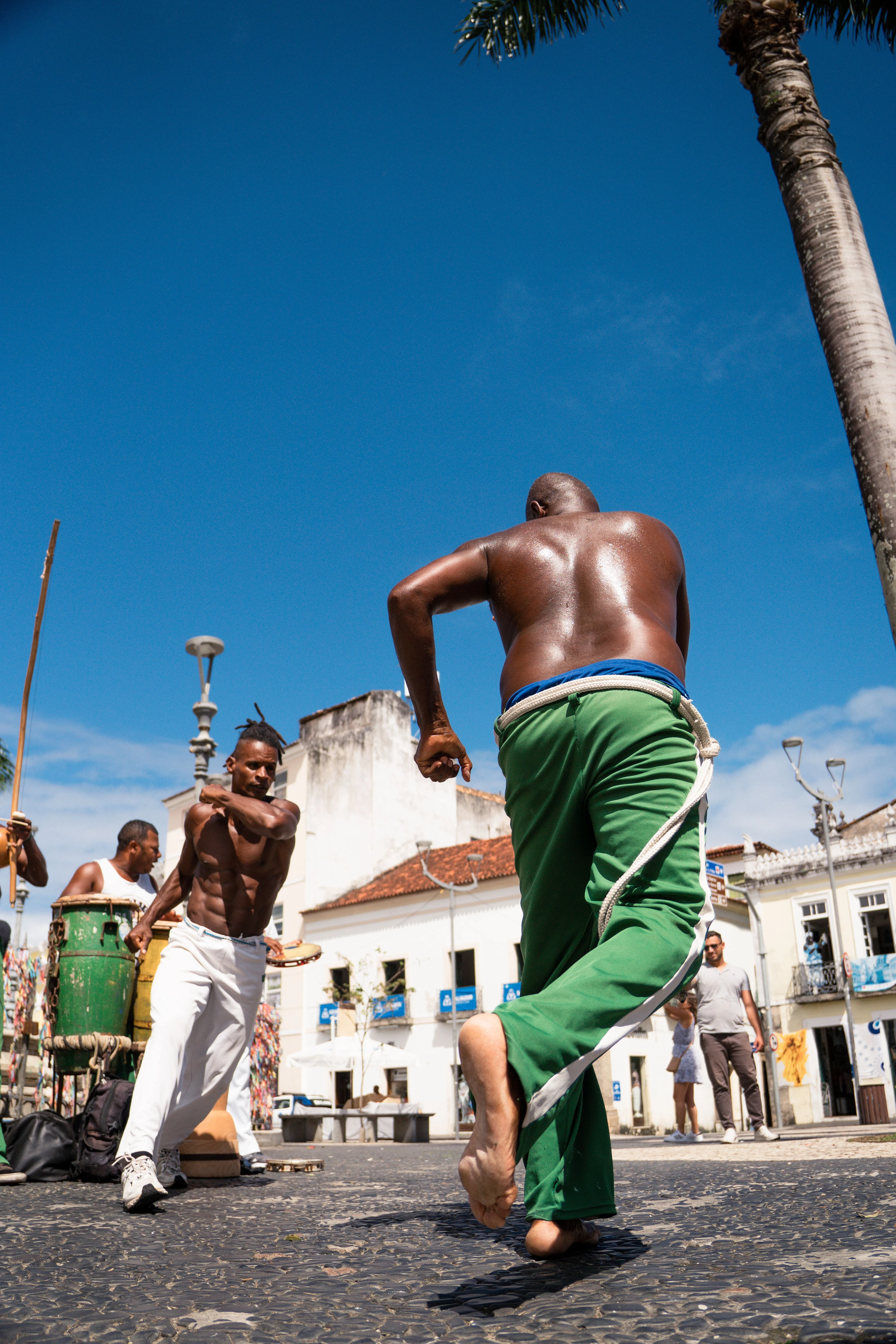 Capoeira players moving at street level beneath a vivid blue Salvador sky
