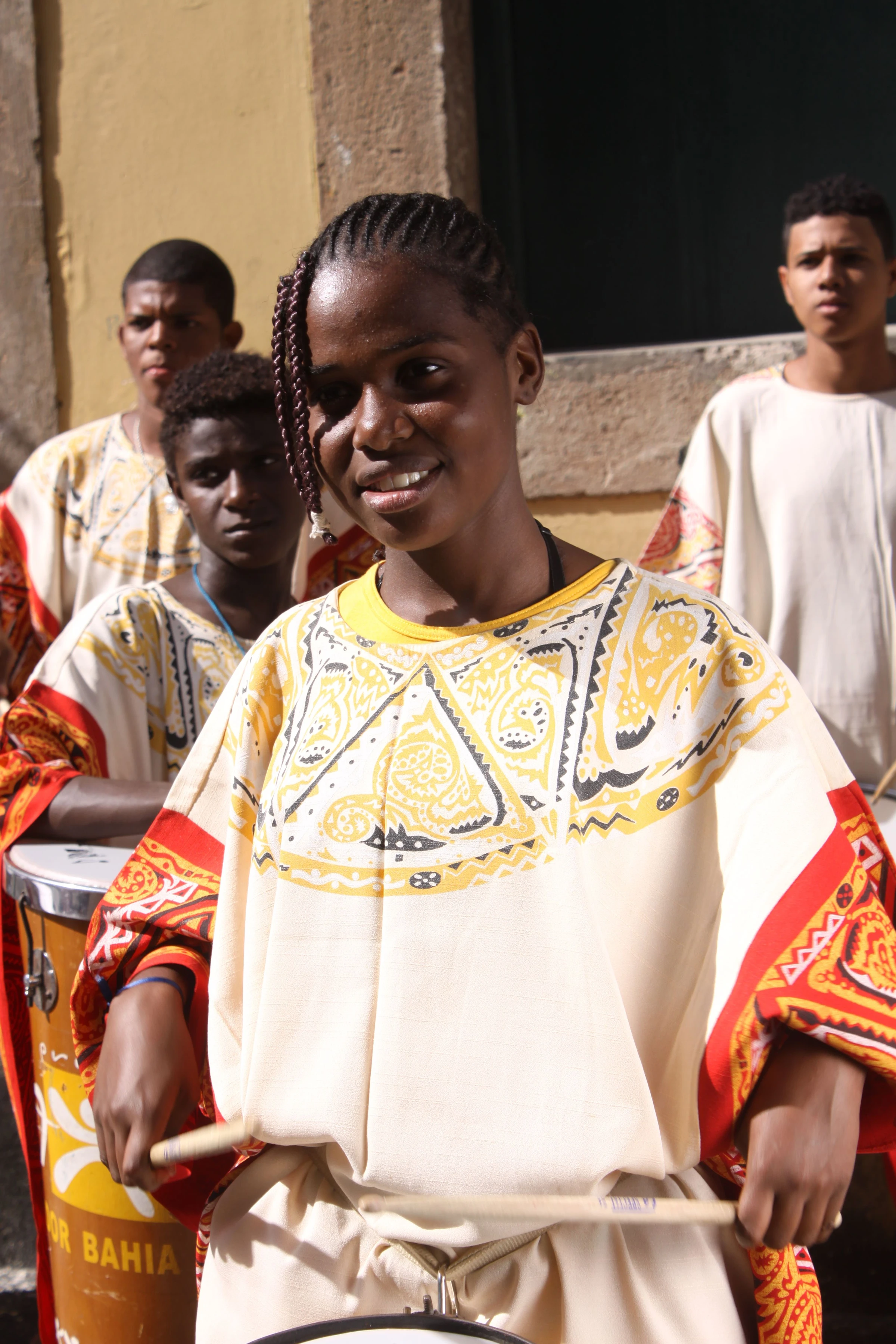 Smiling percussionists in vivid yellow and red clothing at a public event in Salvador