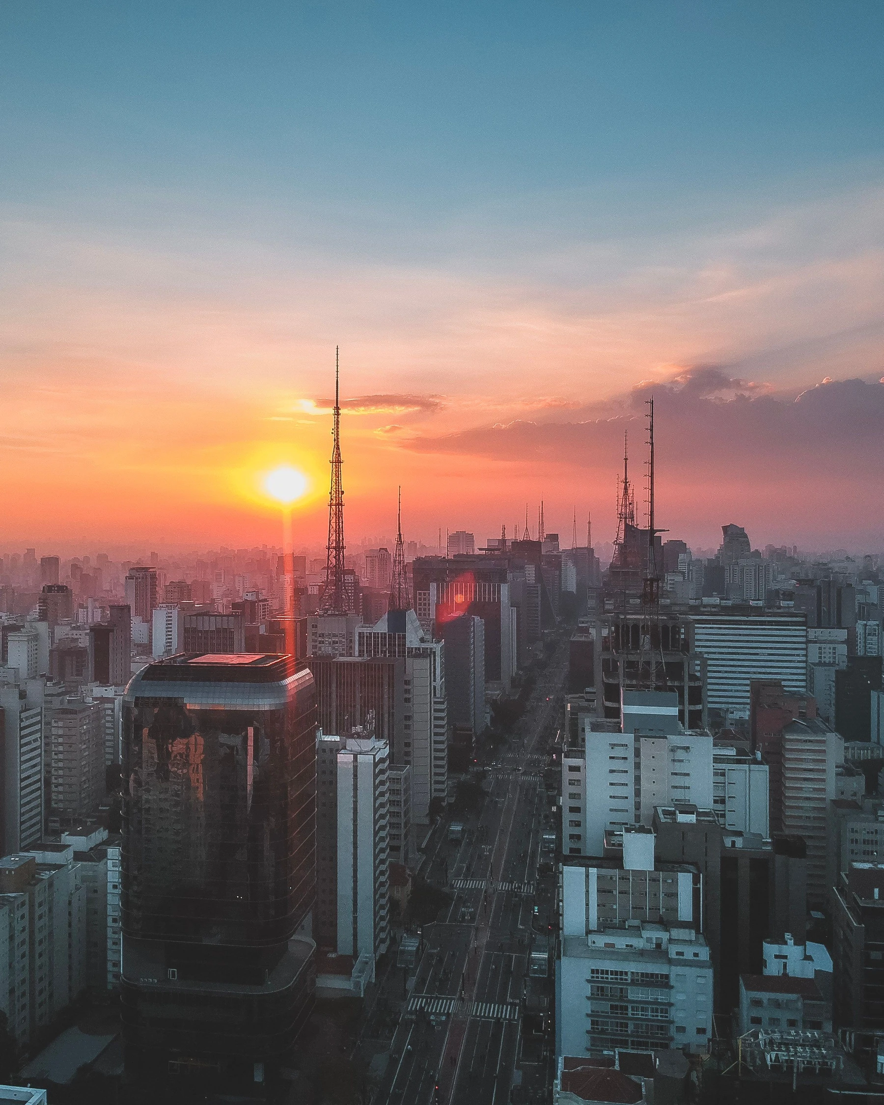 The sun setting beside towers and antennas above Avenida Paulista