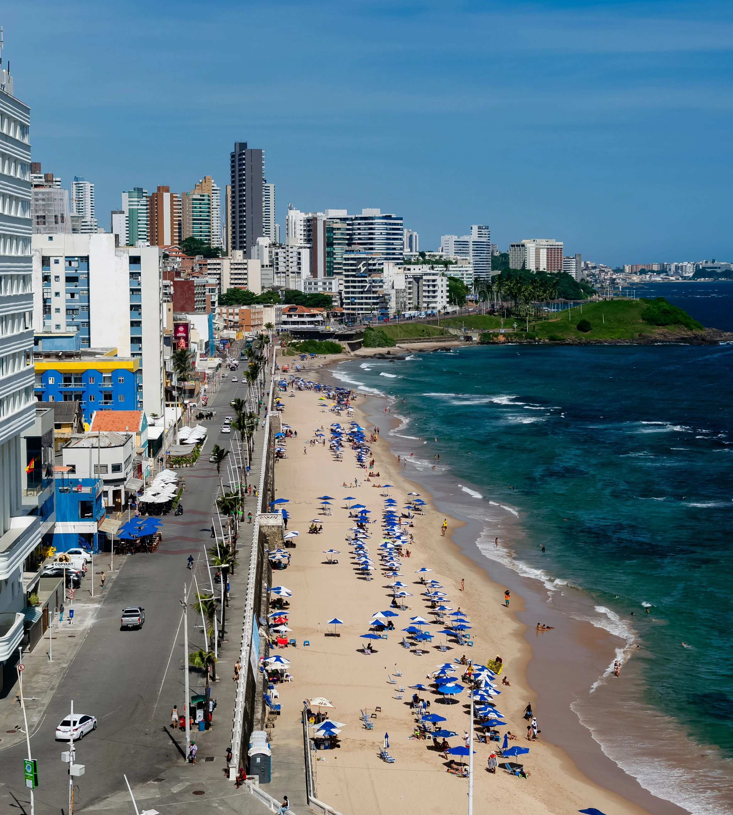 Beach umbrellas, the seafront road and urban buildings line Salvador’s coast.