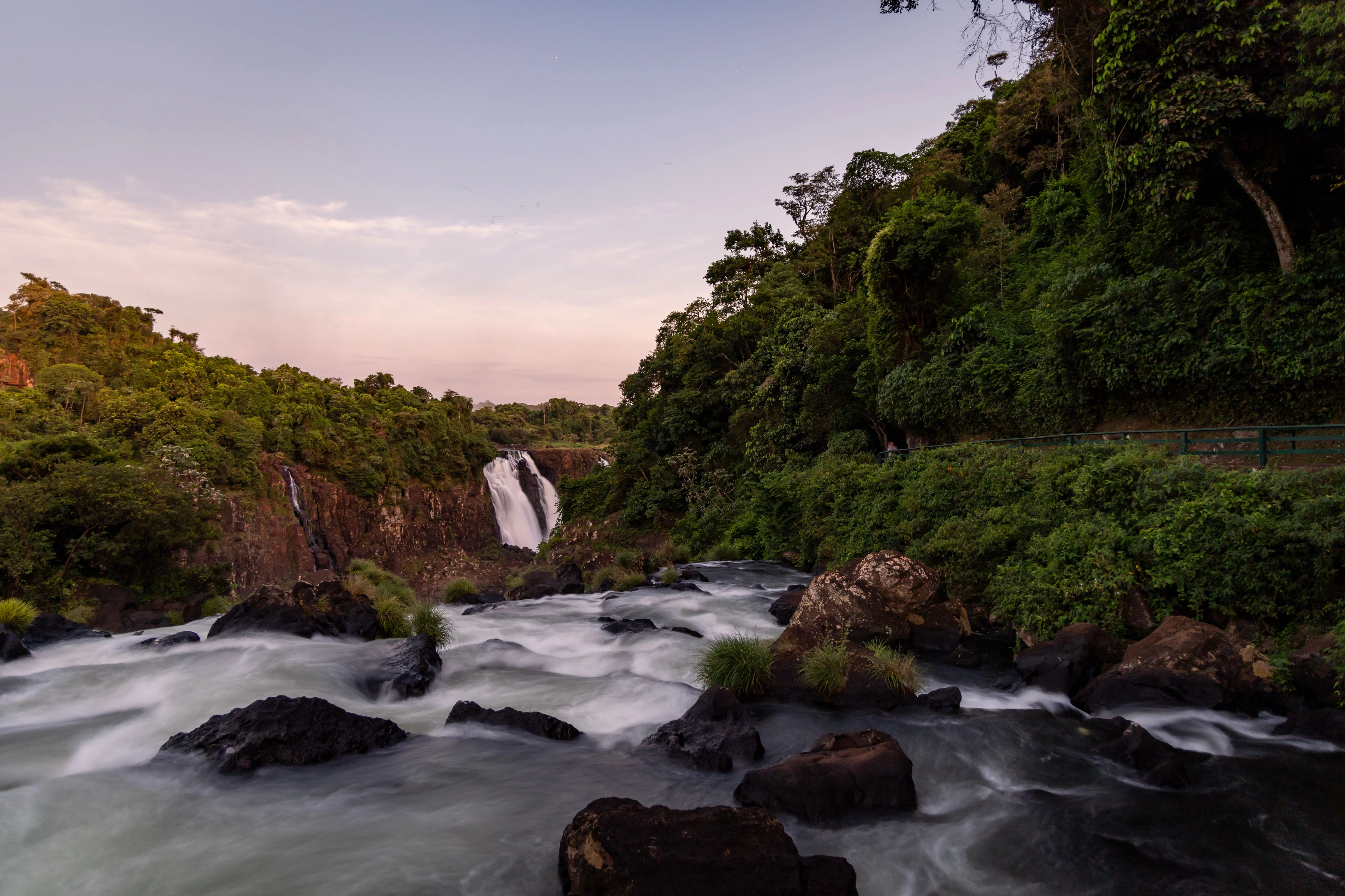 A river flows around dark rocks toward a waterfall beneath a twilight sky in Brazil, shown as landscape context.