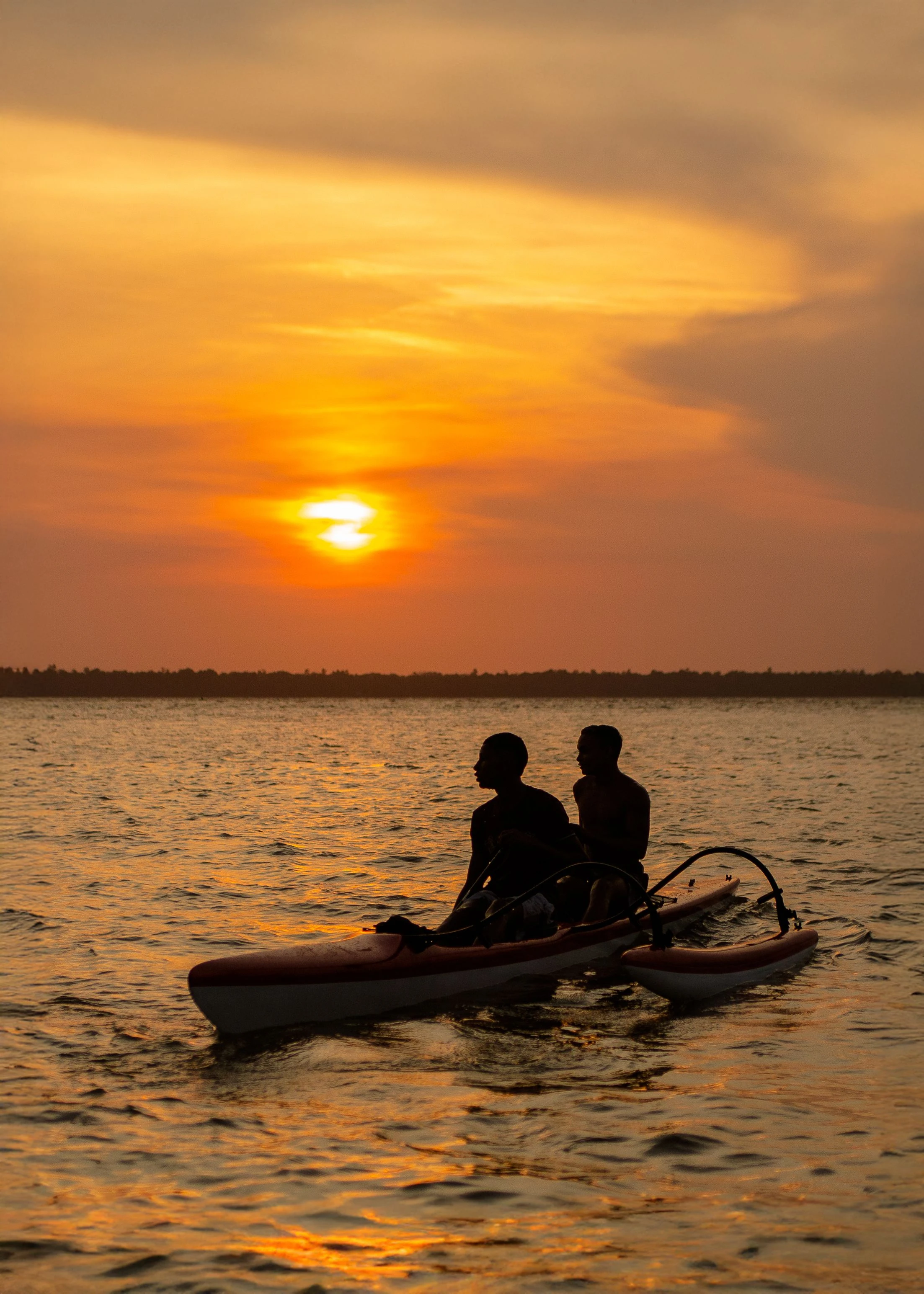 Two people in a canoe silhouetted against orange sunset light near Belém