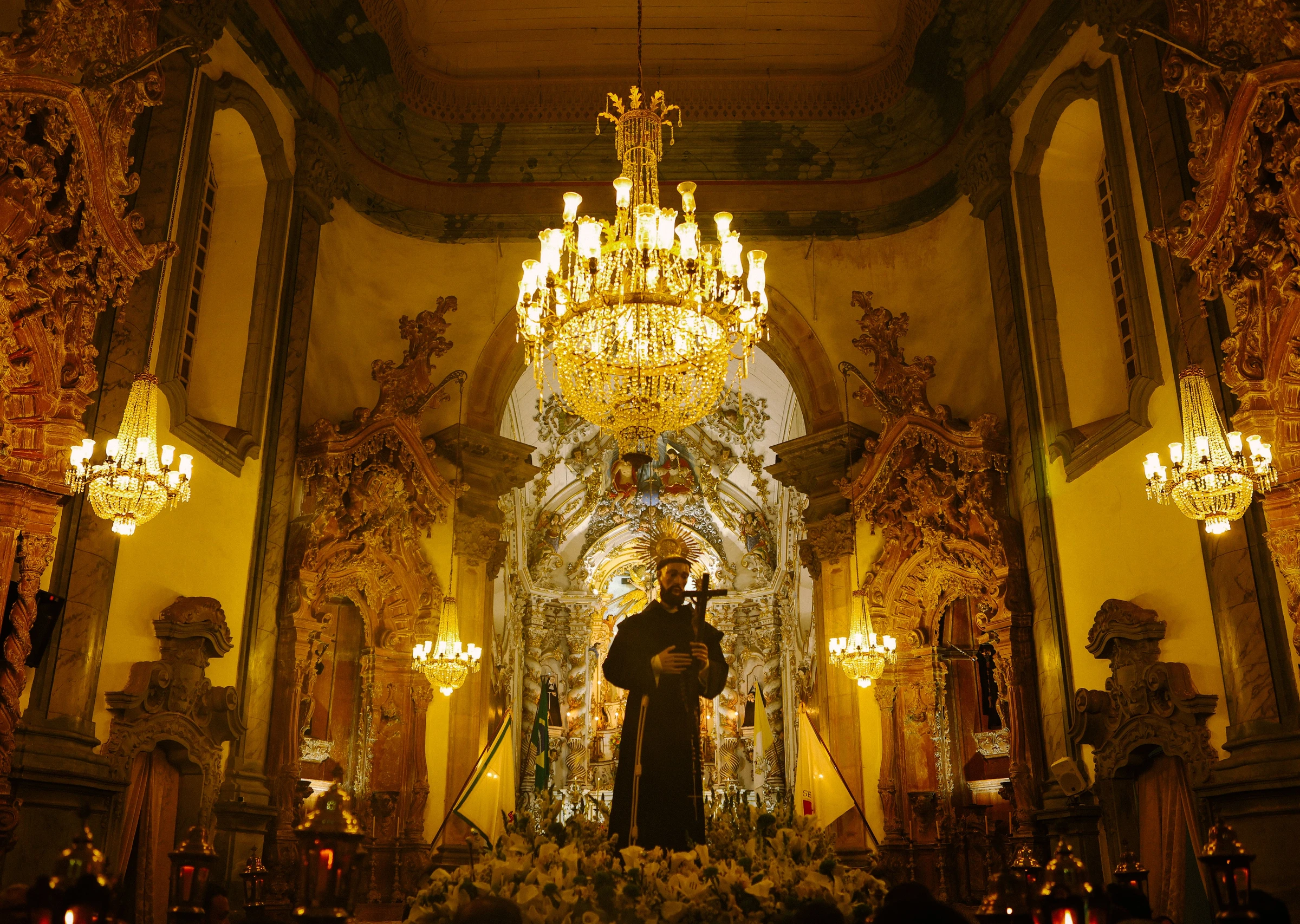An ornate chandelier hangs before richly carved and gilded church decoration in Ouro Preto