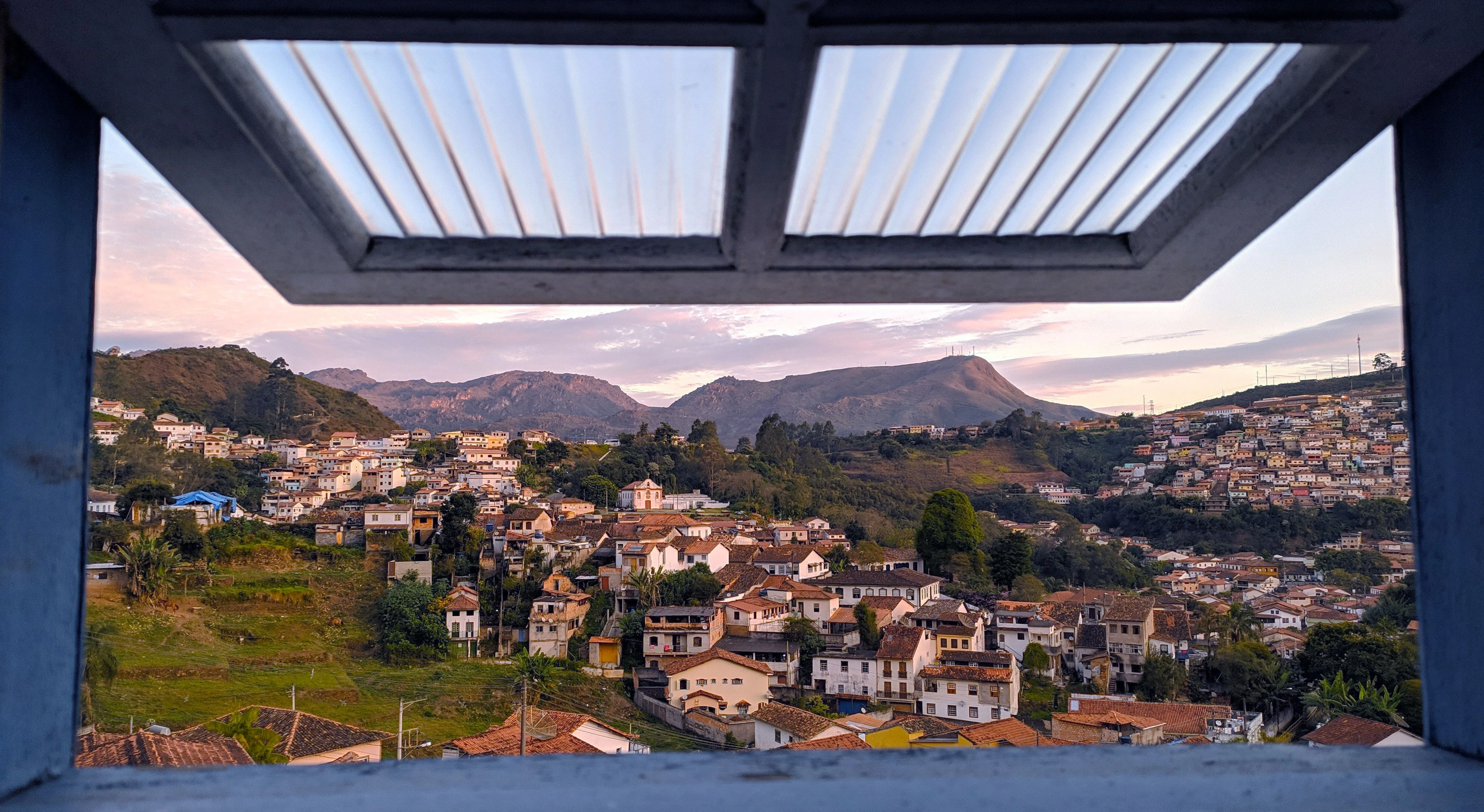 A blue-painted window frames the layered houses and church towers of Ouro Preto