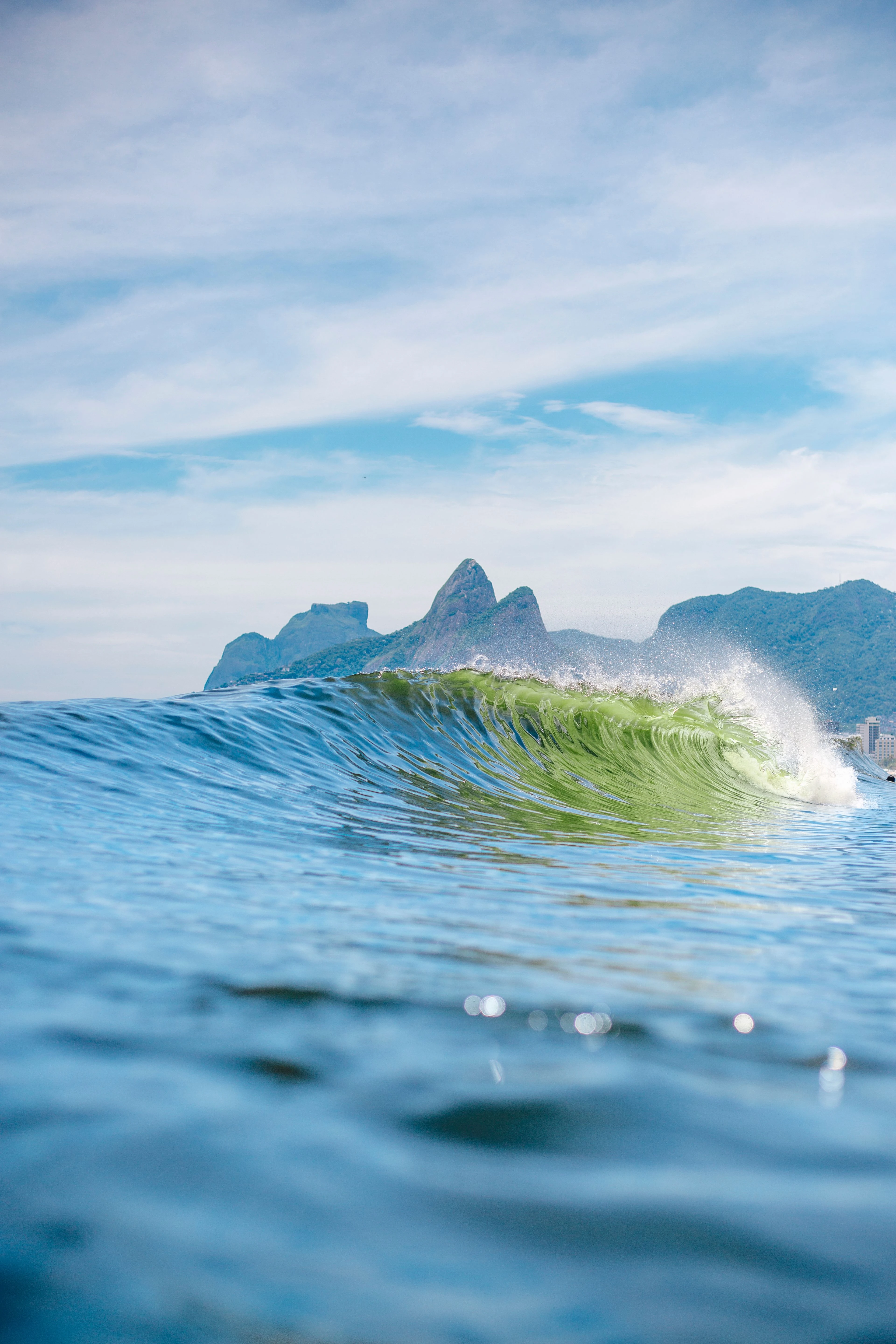 A sunlit green-blue wave rising before Rio’s coastal mountains
