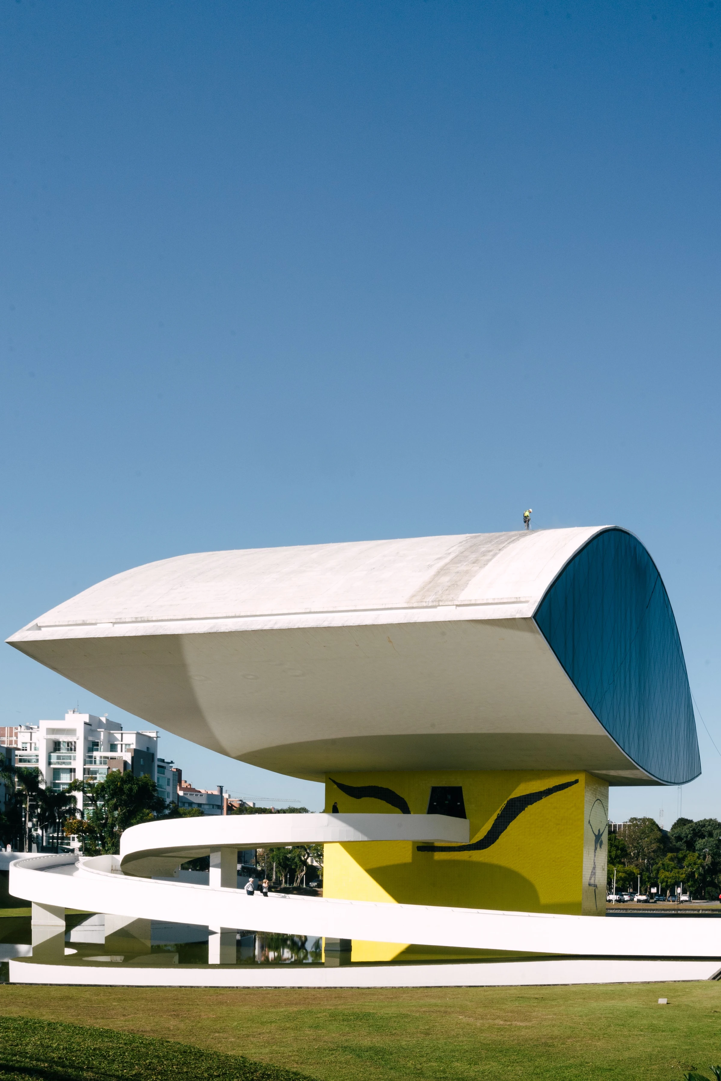 A white curving access ramp coils beside the yellow tiled eye of Museu Oscar Niemeyer.
