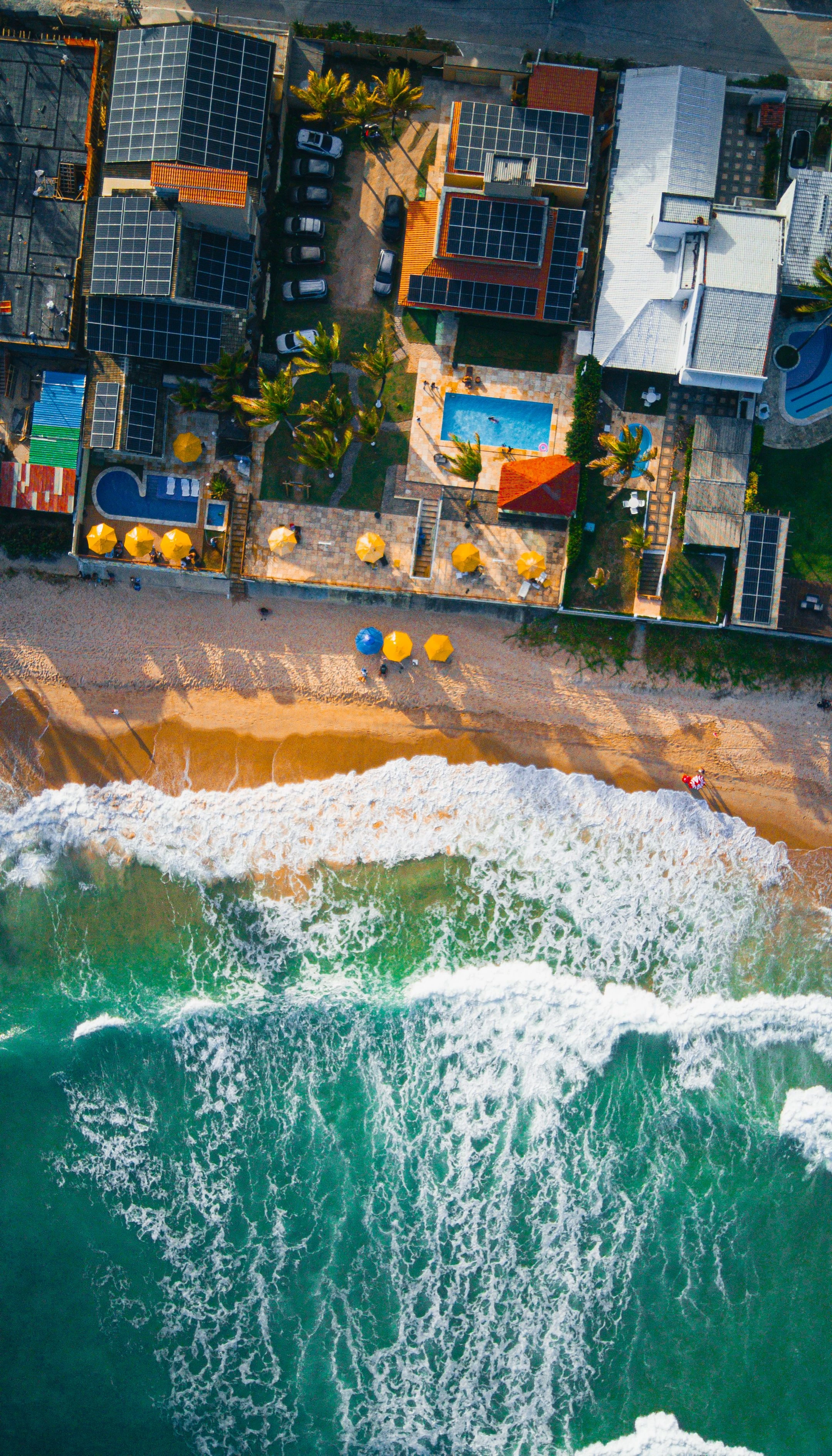 An overhead view of breaking waves, colorful umbrellas and beachfront buildings at Porto de Galinhas