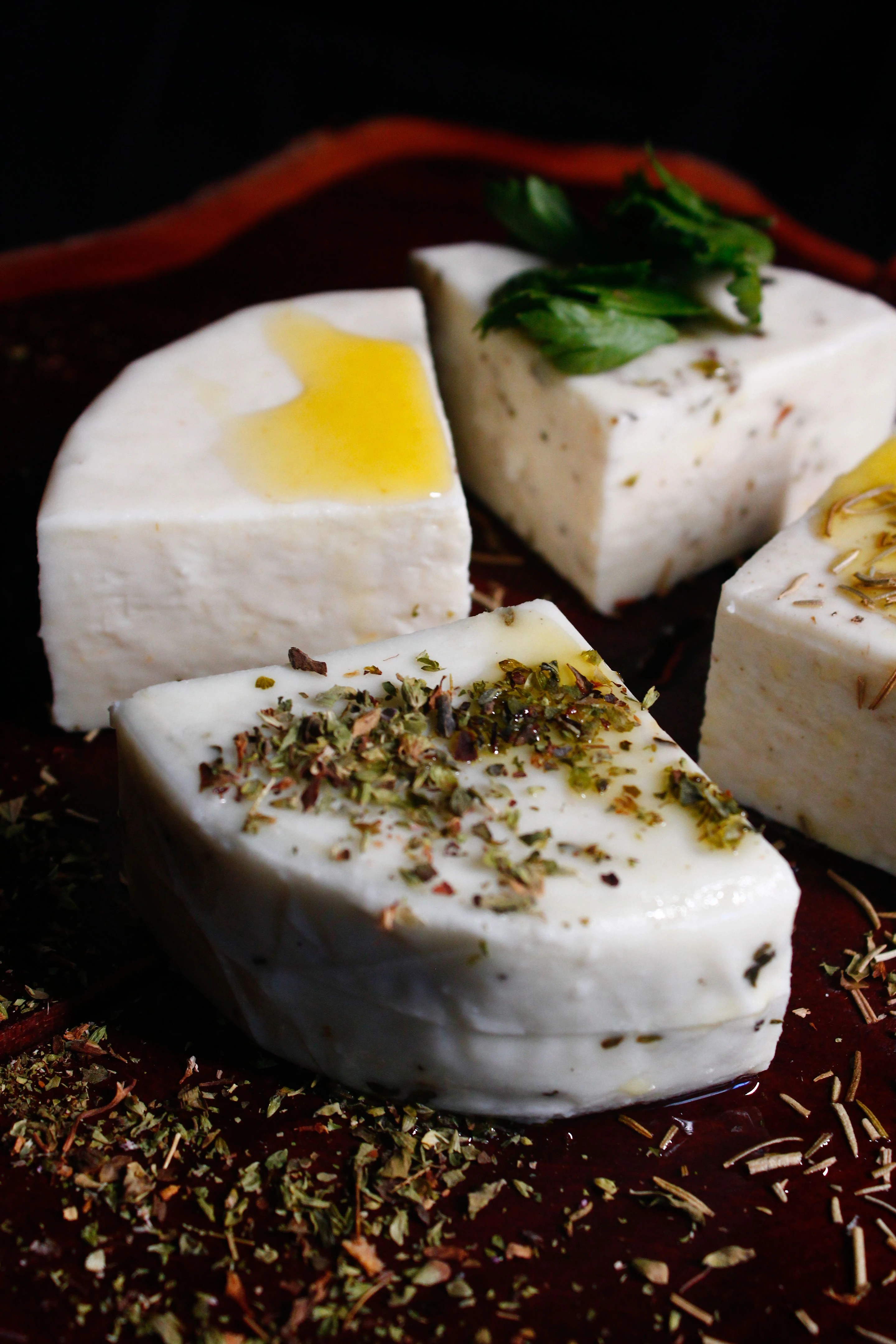 Assorted Brazilian cheeses with herbs and golden oil on a red serving plate