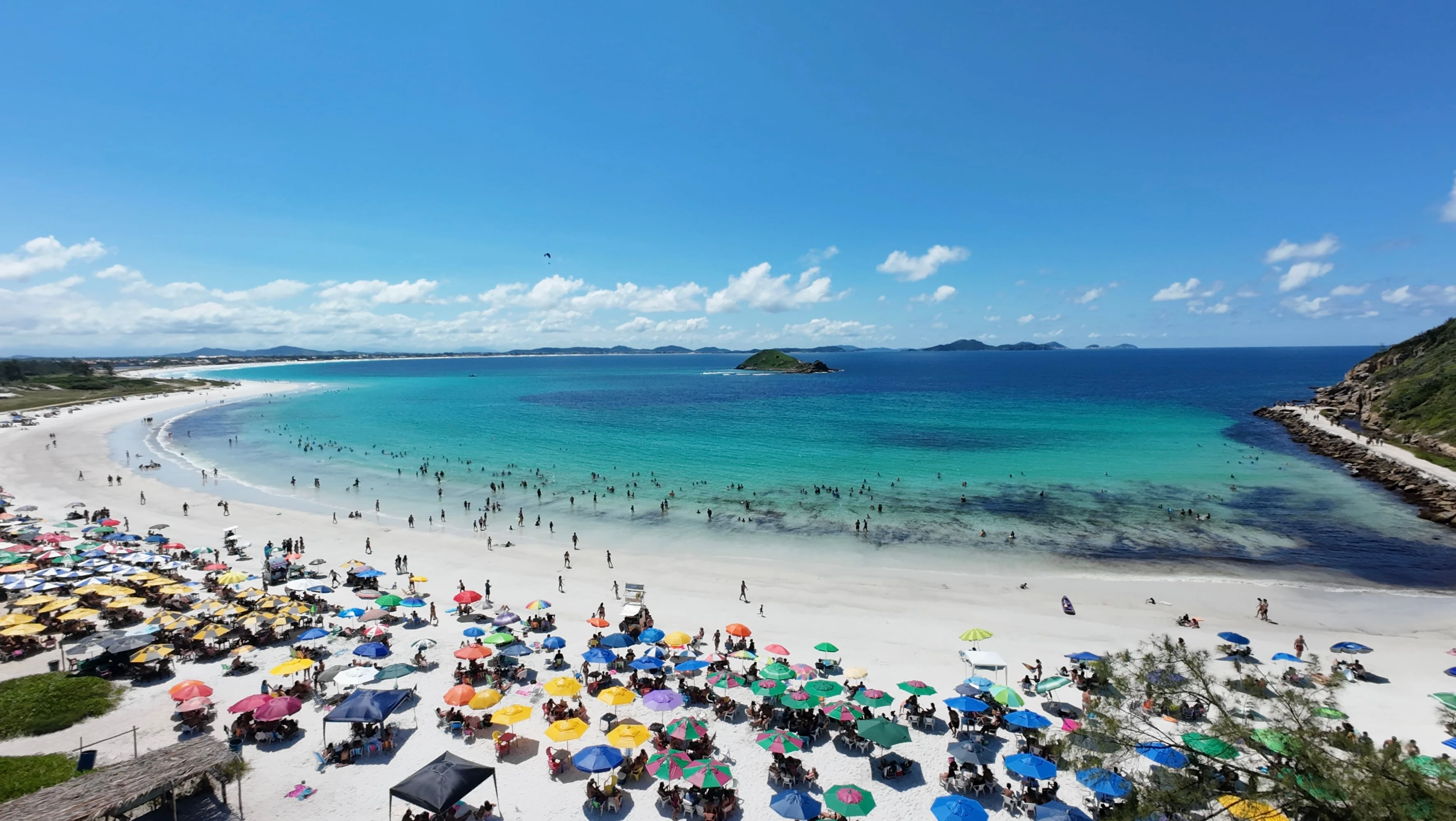 Bright umbrellas and beachgoers beside clear blue water at Pontal do Atalaia