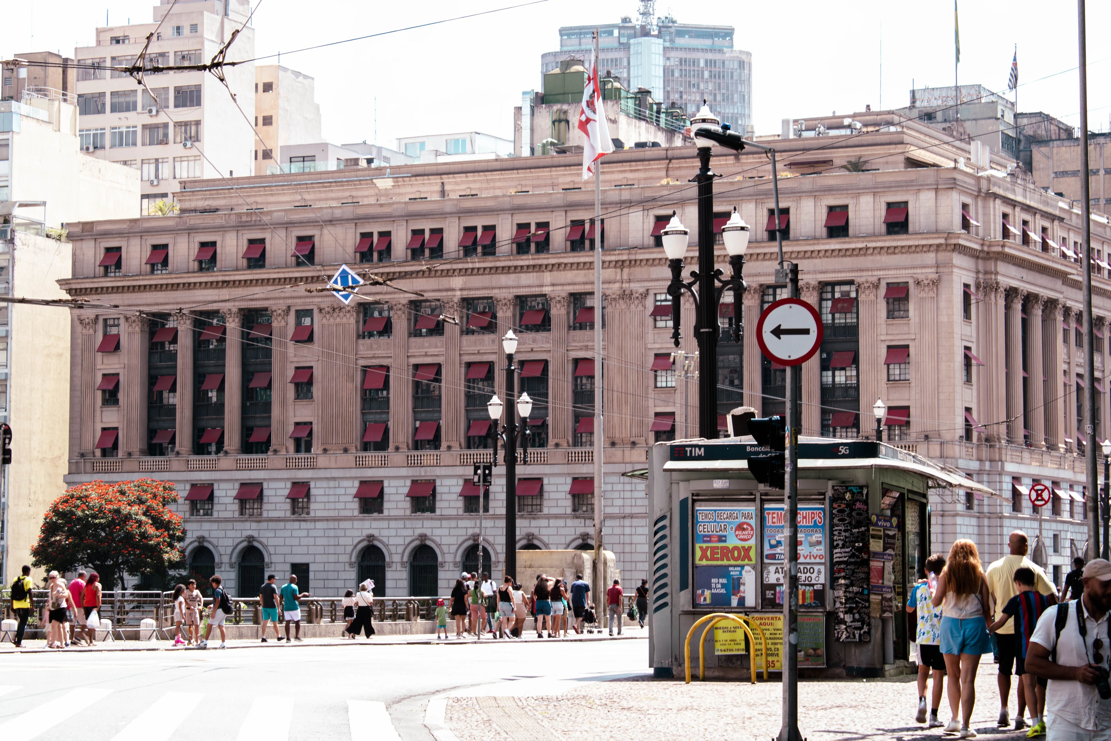 Pedestrians beside a monumental historic façade with rows of red awnings