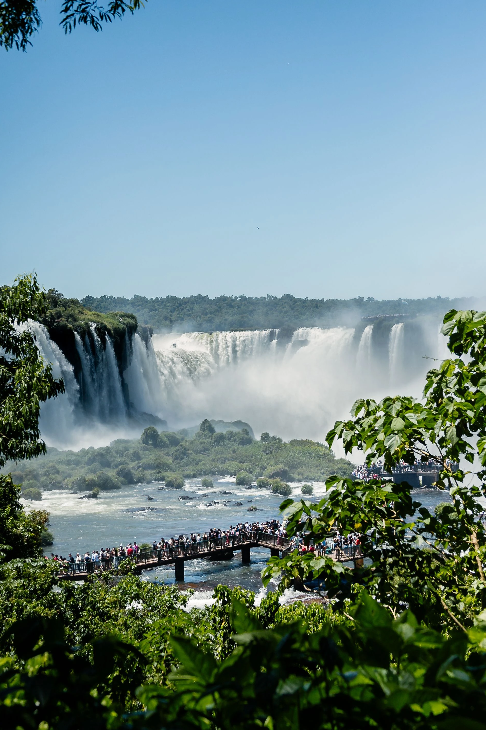 Visitors on the Brazilian walkway beside sunlit cascades and rising spray at Iguaçu Falls.