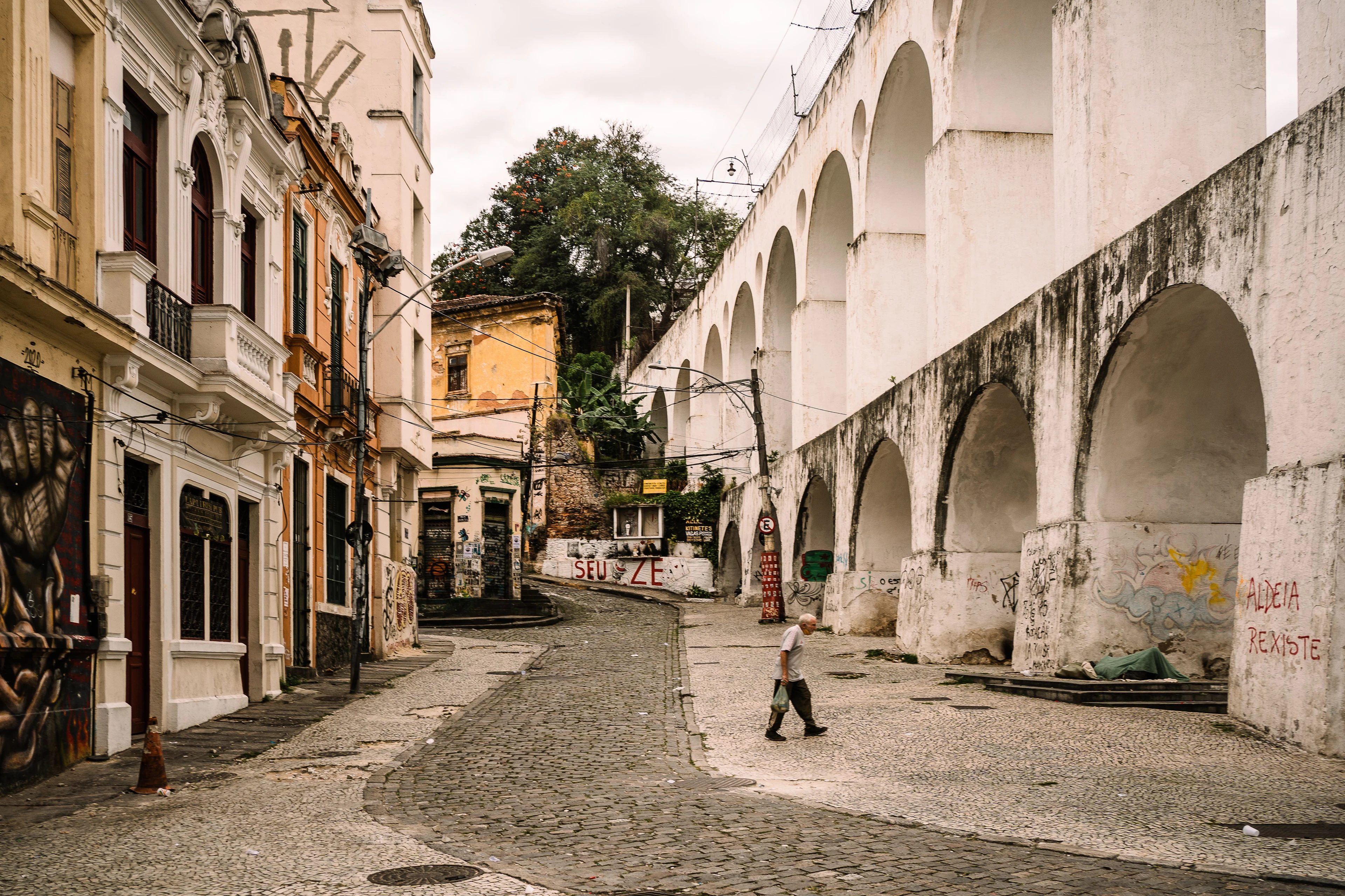 A pedestrian between historic façades and the arches of Lapa’s aqueduct