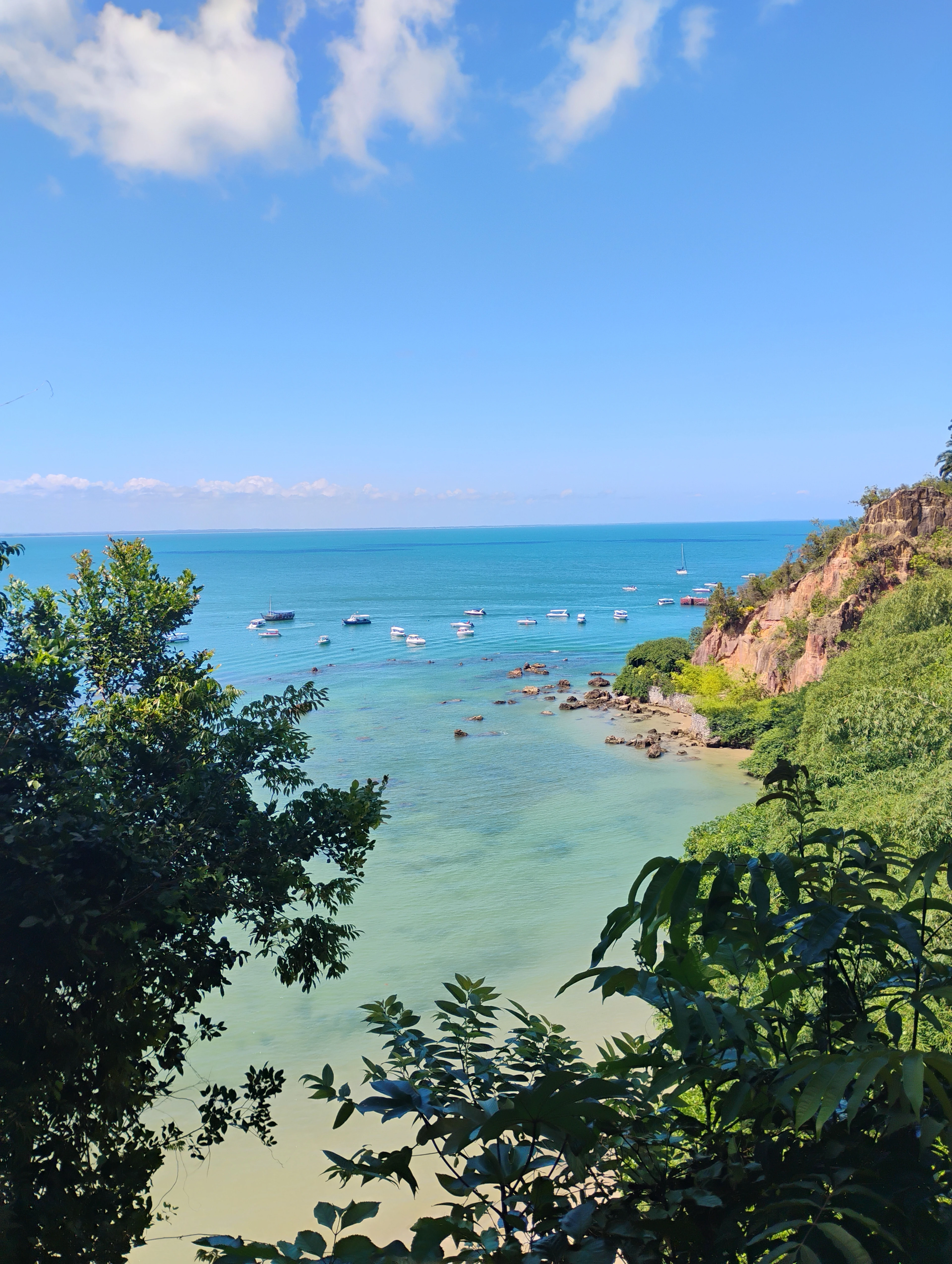 A high coastal view frames cliffs, trees and boats on blue water