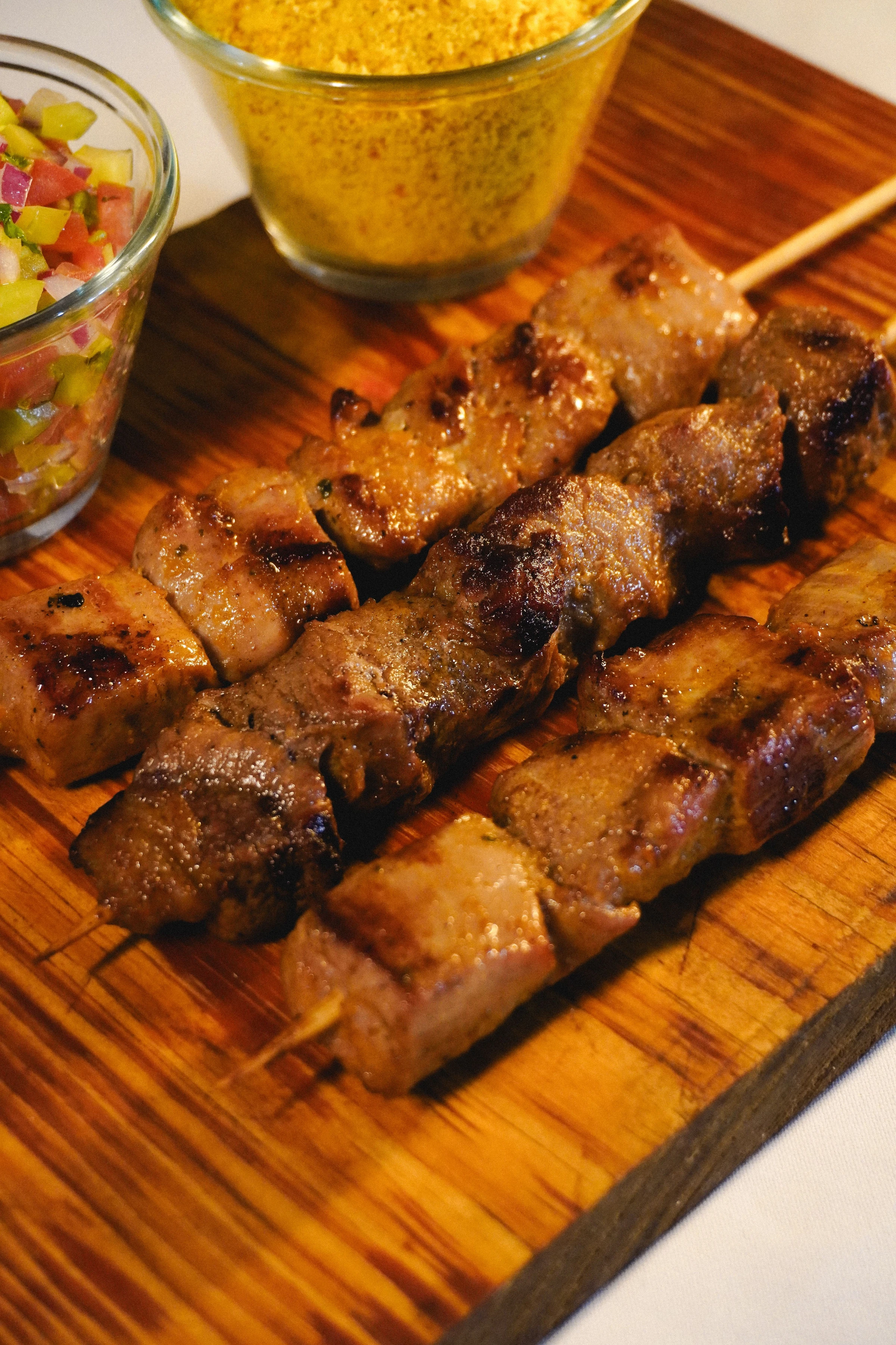 Grilled skewers served with colorful vinaigrette and golden farofa on a wooden board in Rio Grande do Norte.