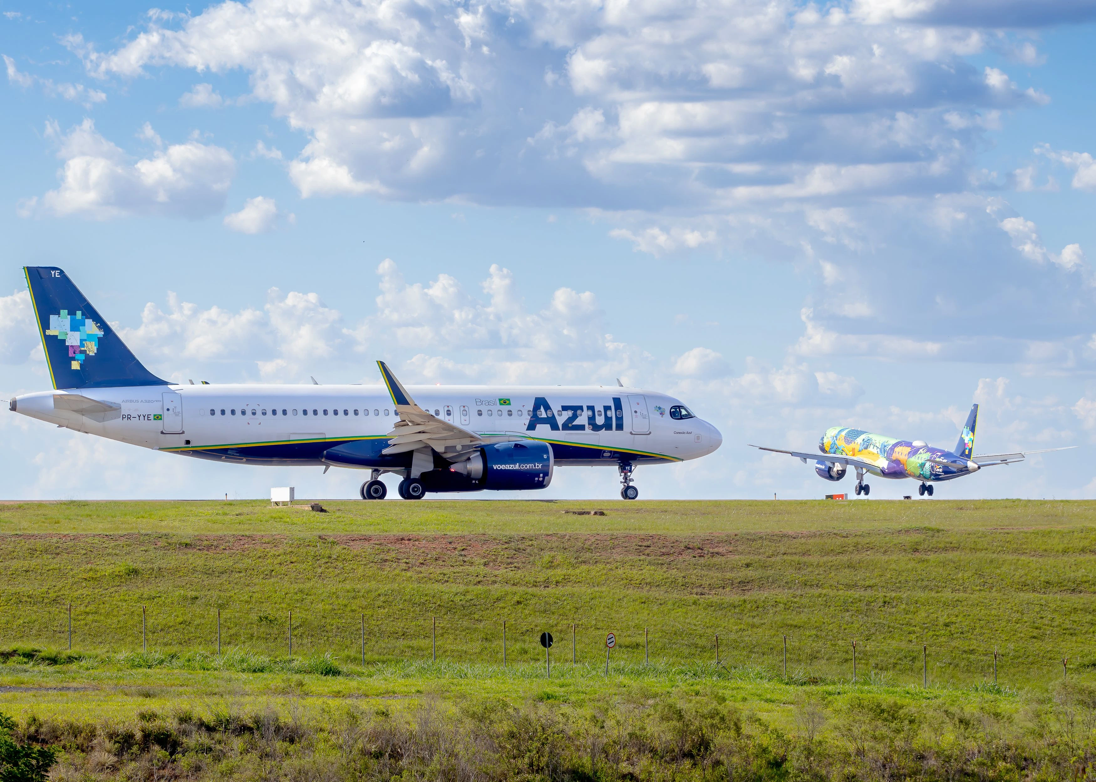 Two Azul aircraft on a Brazilian runway beneath sunlit clouds