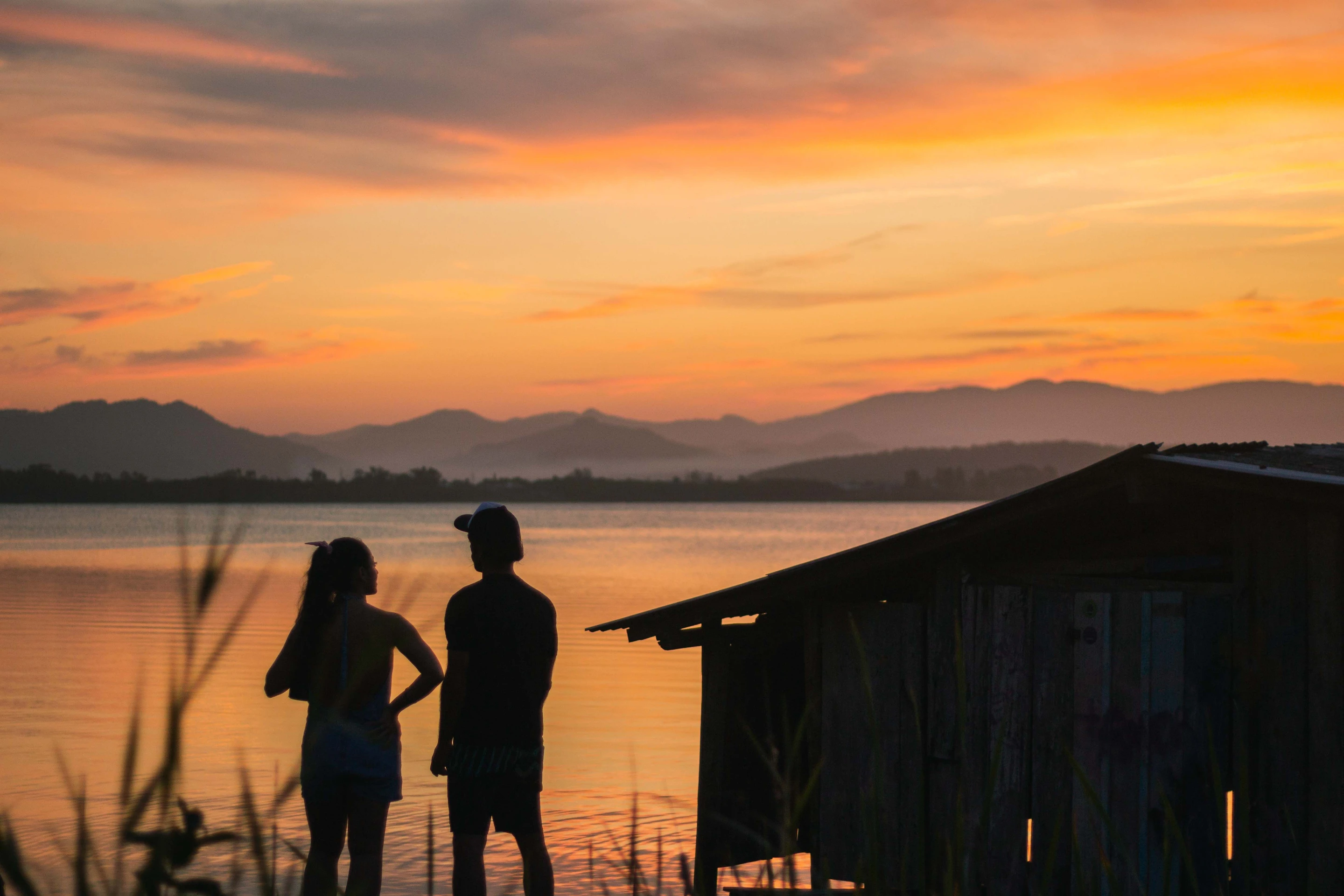 People stand beside the water under an orange Florianópolis sunset.