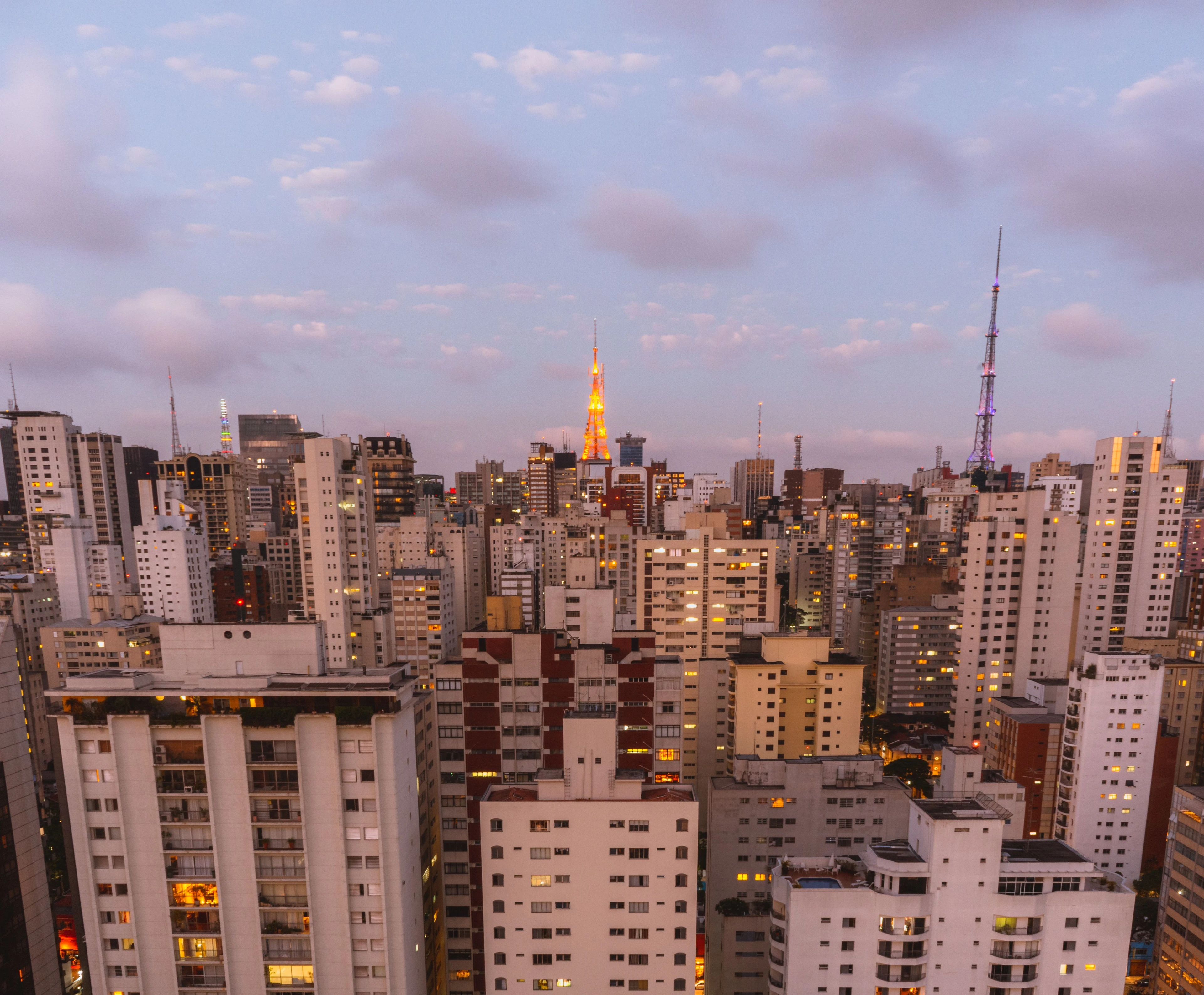 Illuminated São Paulo buildings and antenna towers beneath a twilight sky