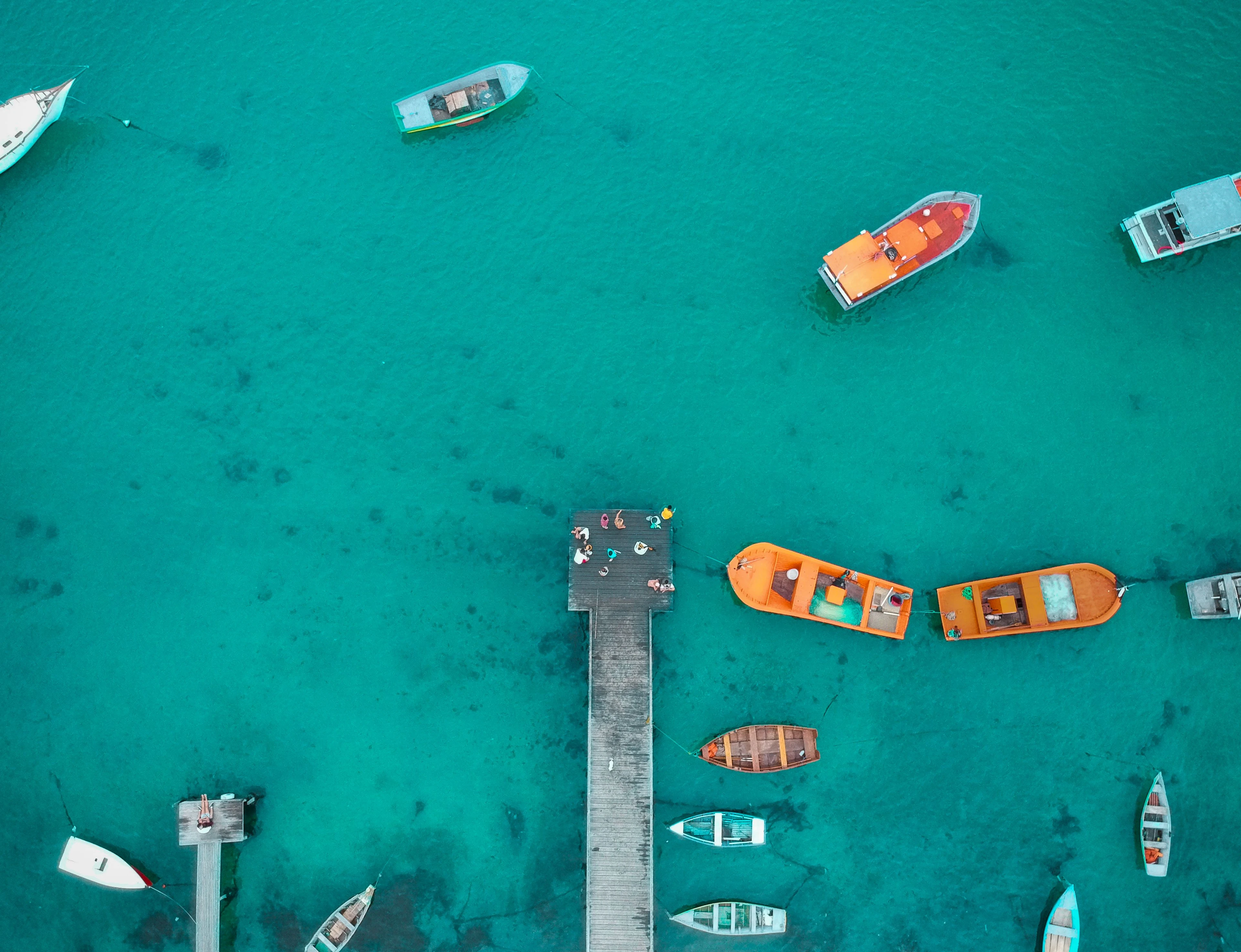 Orange and wooden boats gather beside a pier in clear coastal water