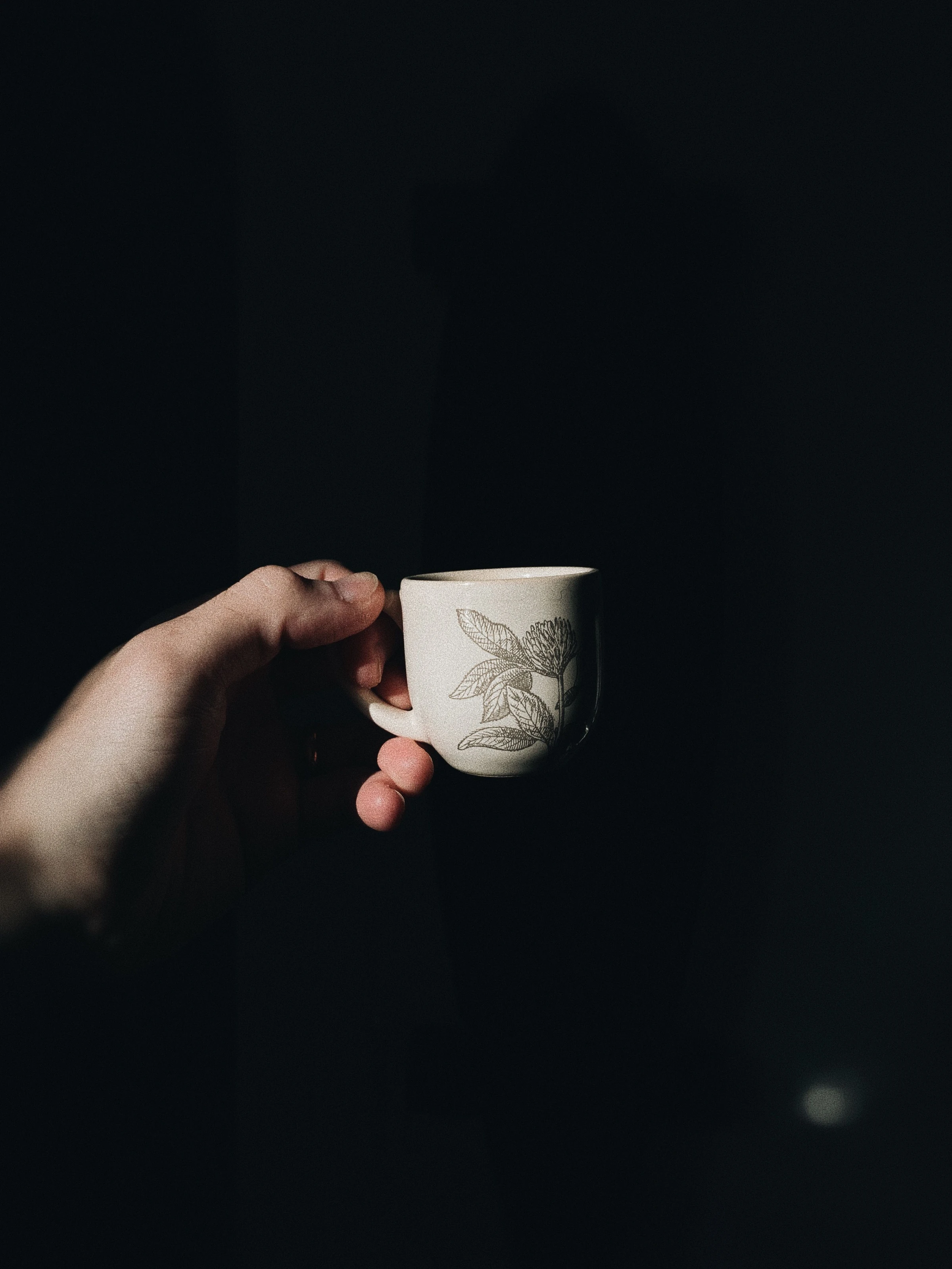 A hand holds a patterned coffee cup in a shaft of light in São Paulo.