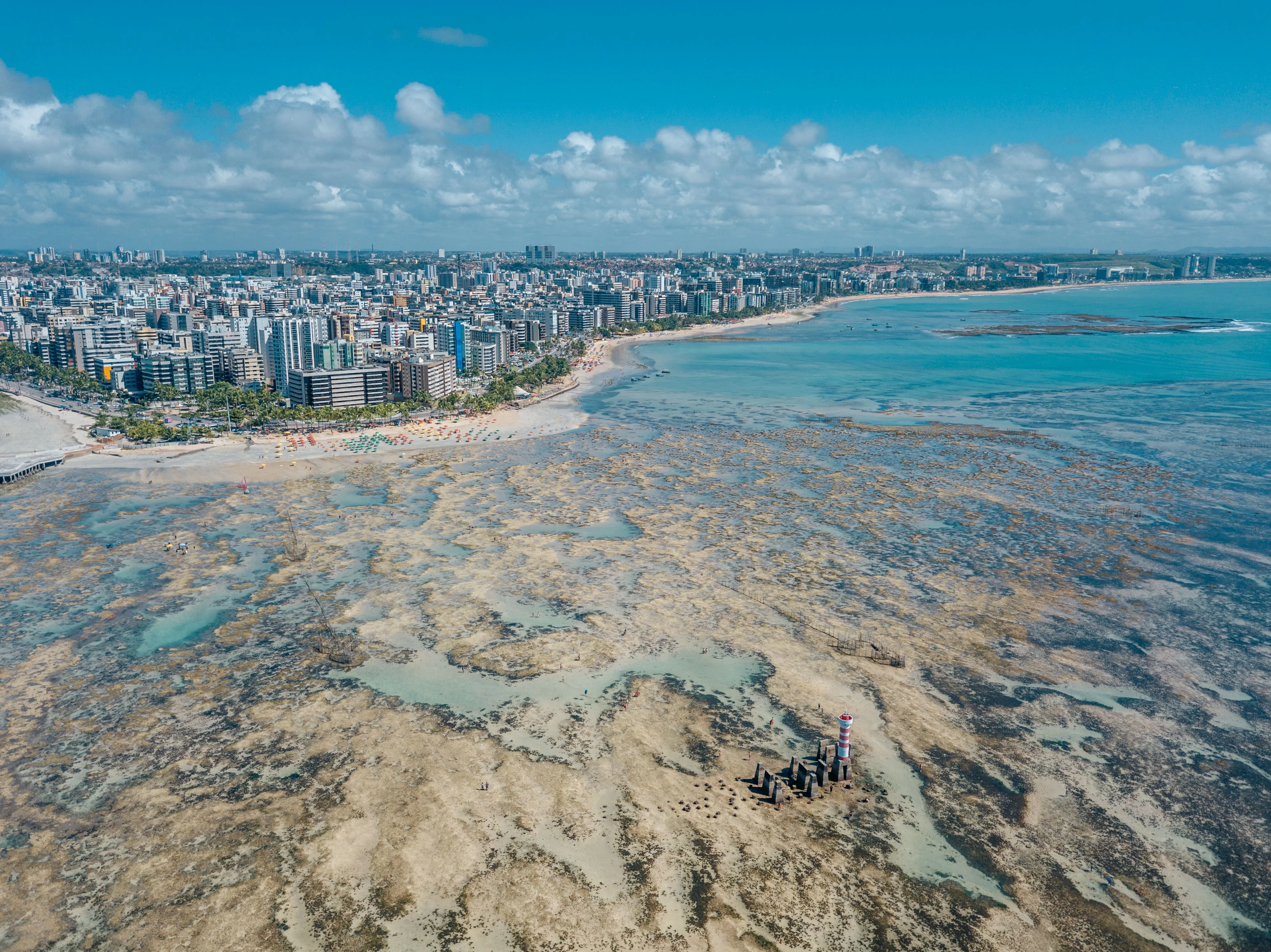 A sweeping view of Maceió’s Ponta Verde coast, offshore reef and city buildings