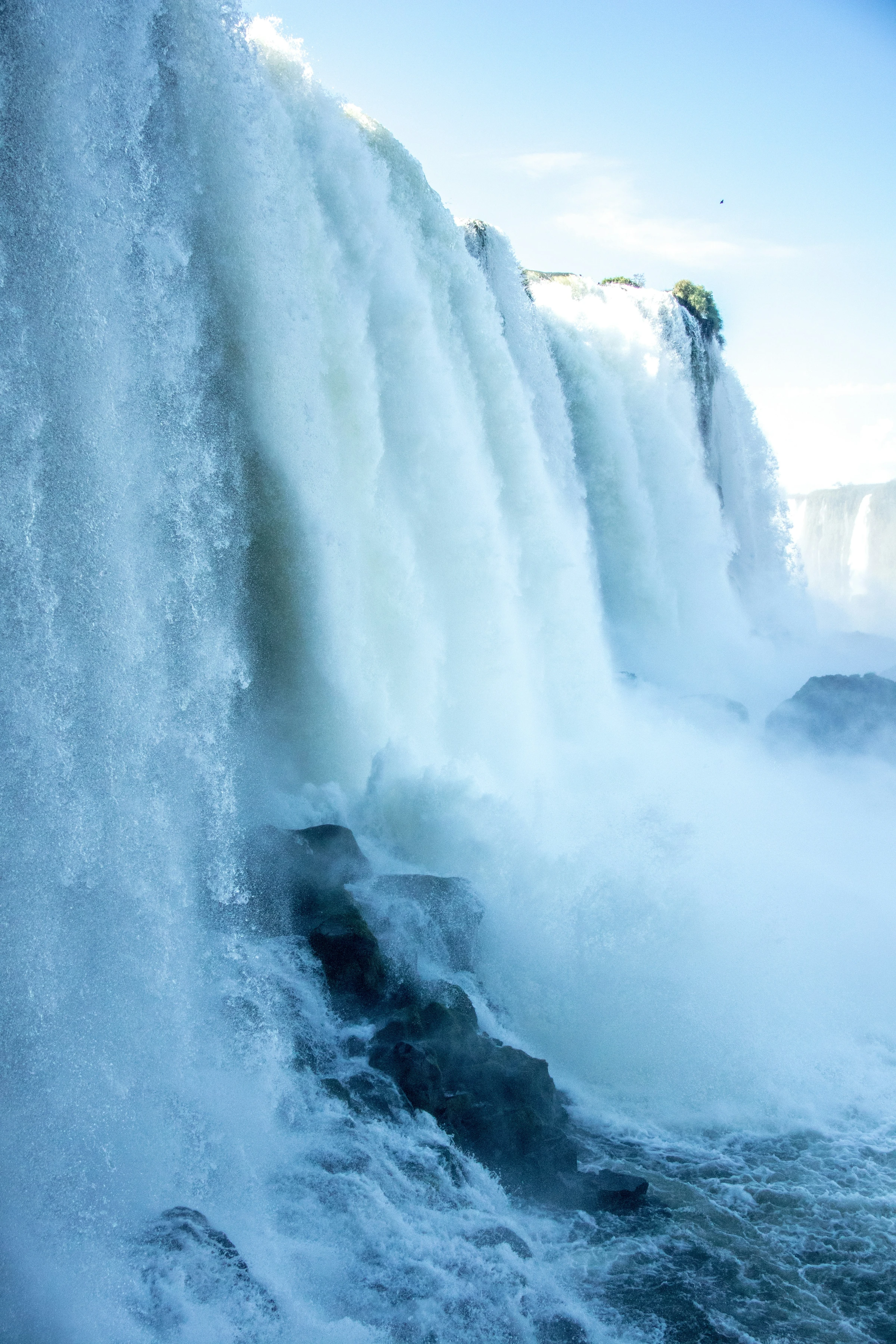 A powerful curtain of water drops into sparkling spray beneath a bright sky at the Brazilian falls.